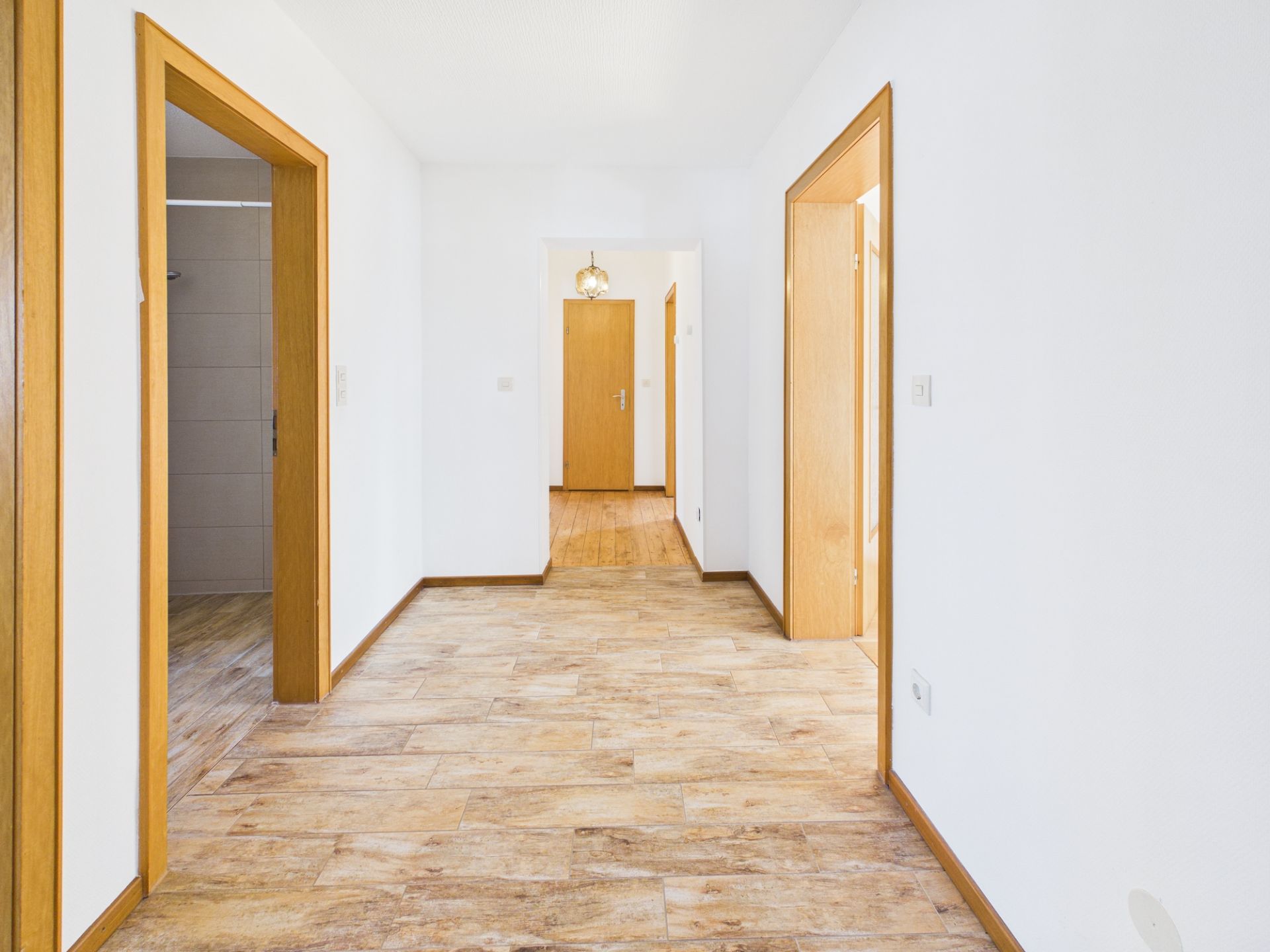 Heller Flur mit Holztüren, Fliesenboden und weißen Wänden in einer Wohnung.
