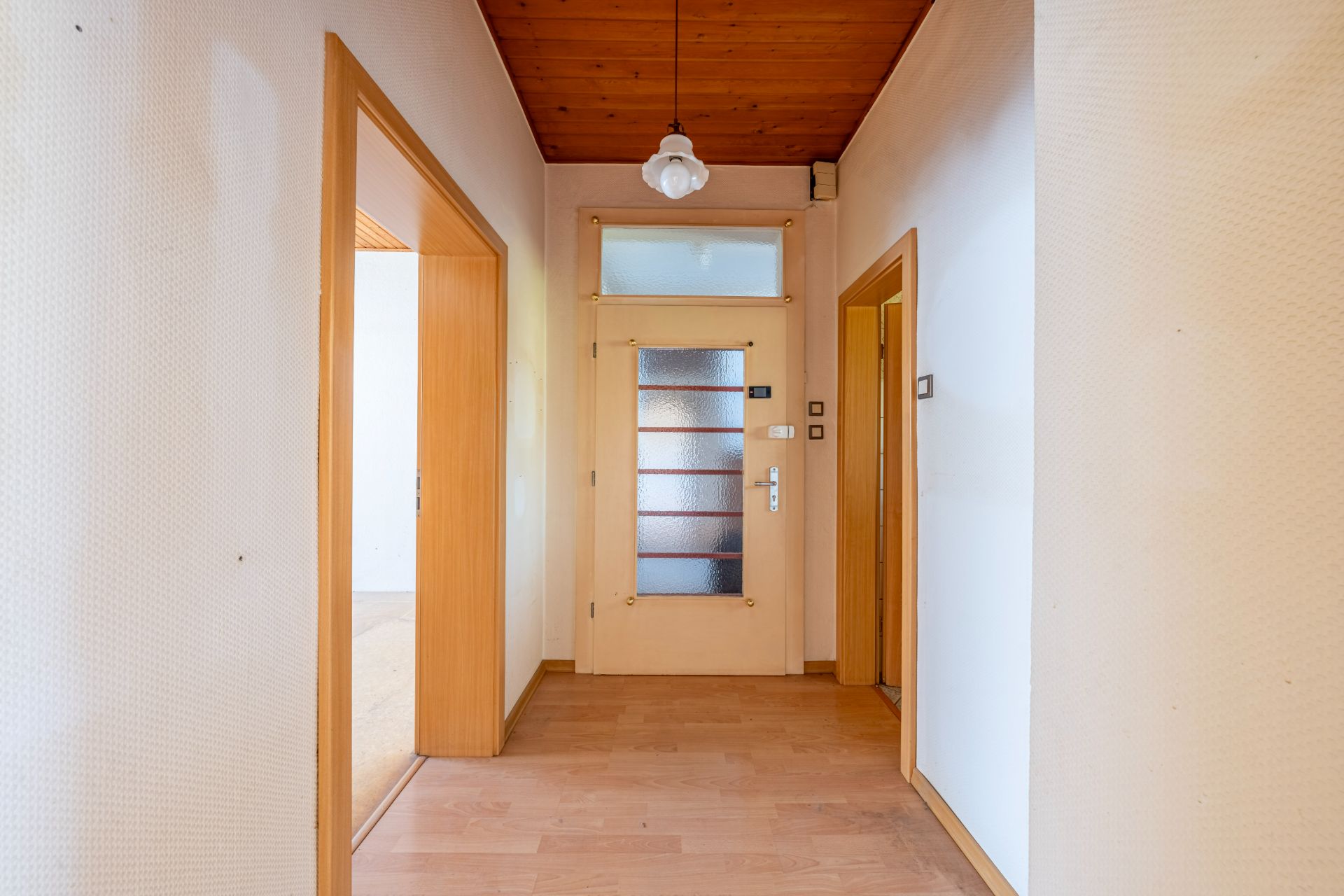 Heller Flur mit Holzboden, Holztüren und Deckenleuchte in einem Wohnhaus.