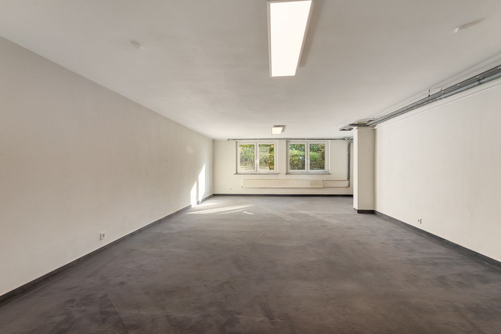 Leerer, heller Raum mit drei Fenstern, weißen Wänden und dunklem Boden.