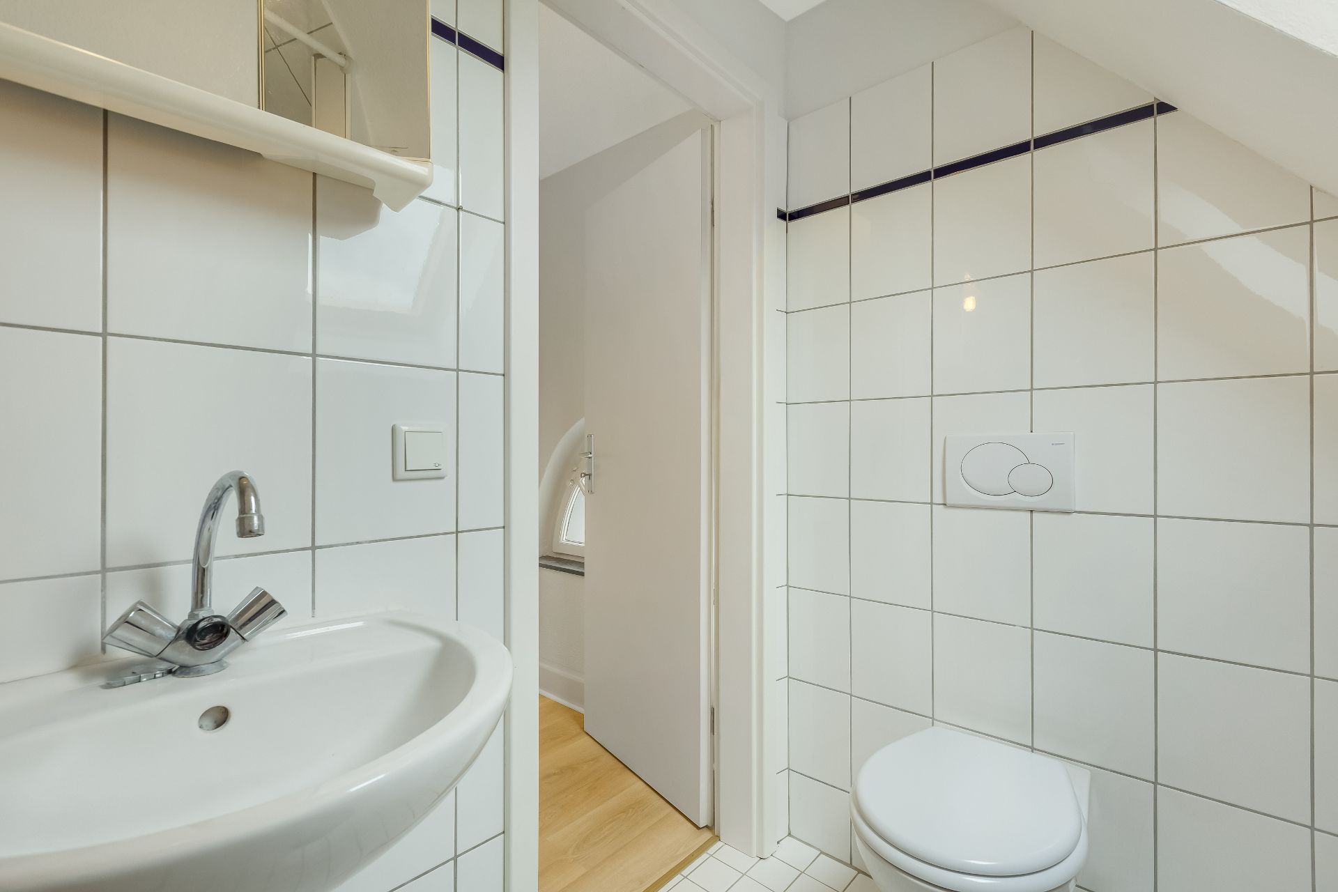 Kleines Badezimmer mit Waschbecken, Spiegel und Toilette, weiße Fliesen an den Wänden.