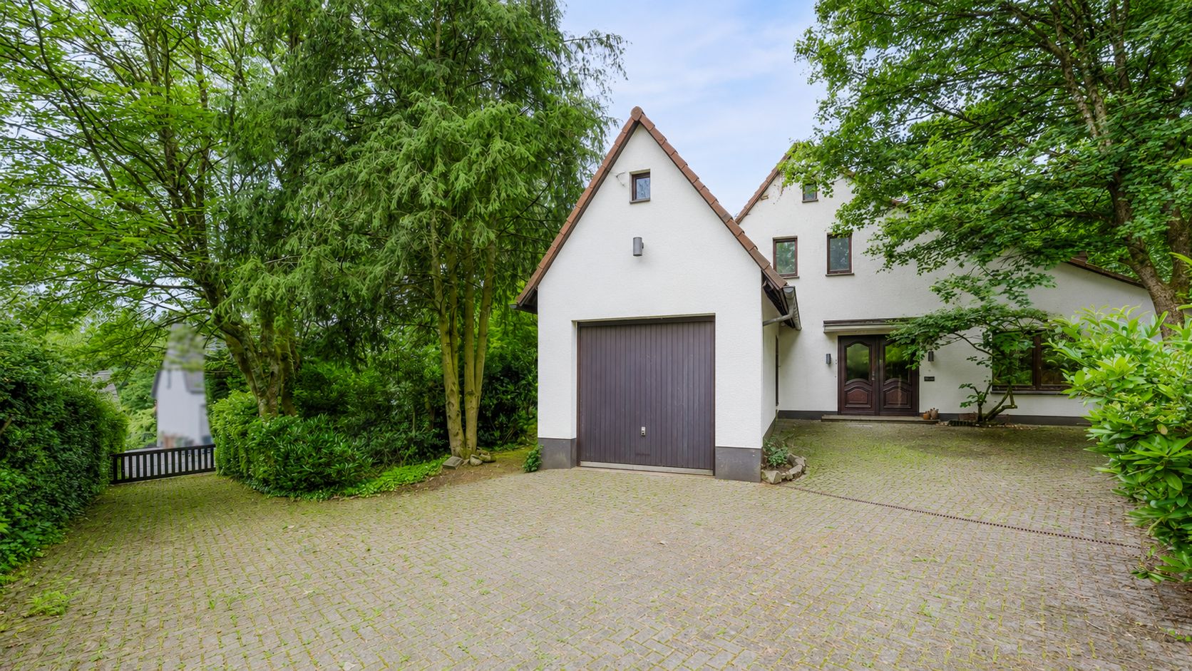 Einfamilienhaus mit Garage, gepflasterter Einfahrt und umgeben von Bäumen.