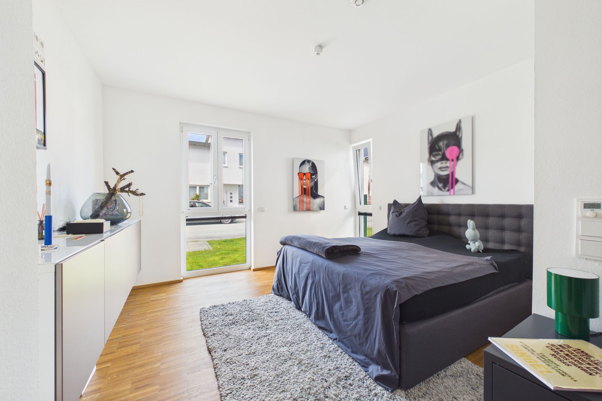 Modernes Schlafzimmer mit großem Bett, Teppich, zwei Fenstern und dekorativen Bildern an den Wänden.