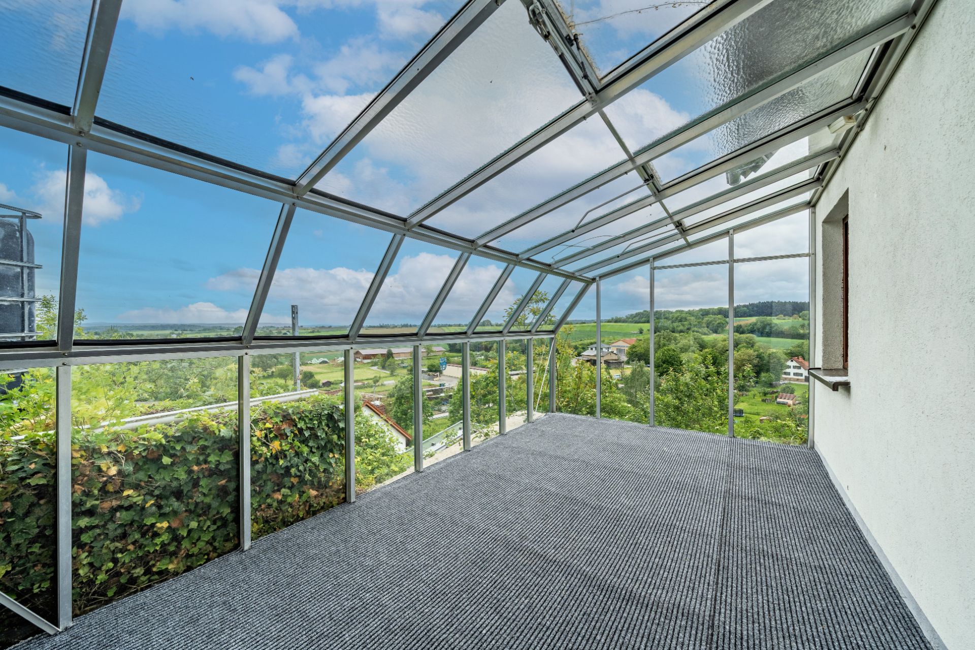 Veranda mit Glasdach und Blick auf grüne Landschaft.