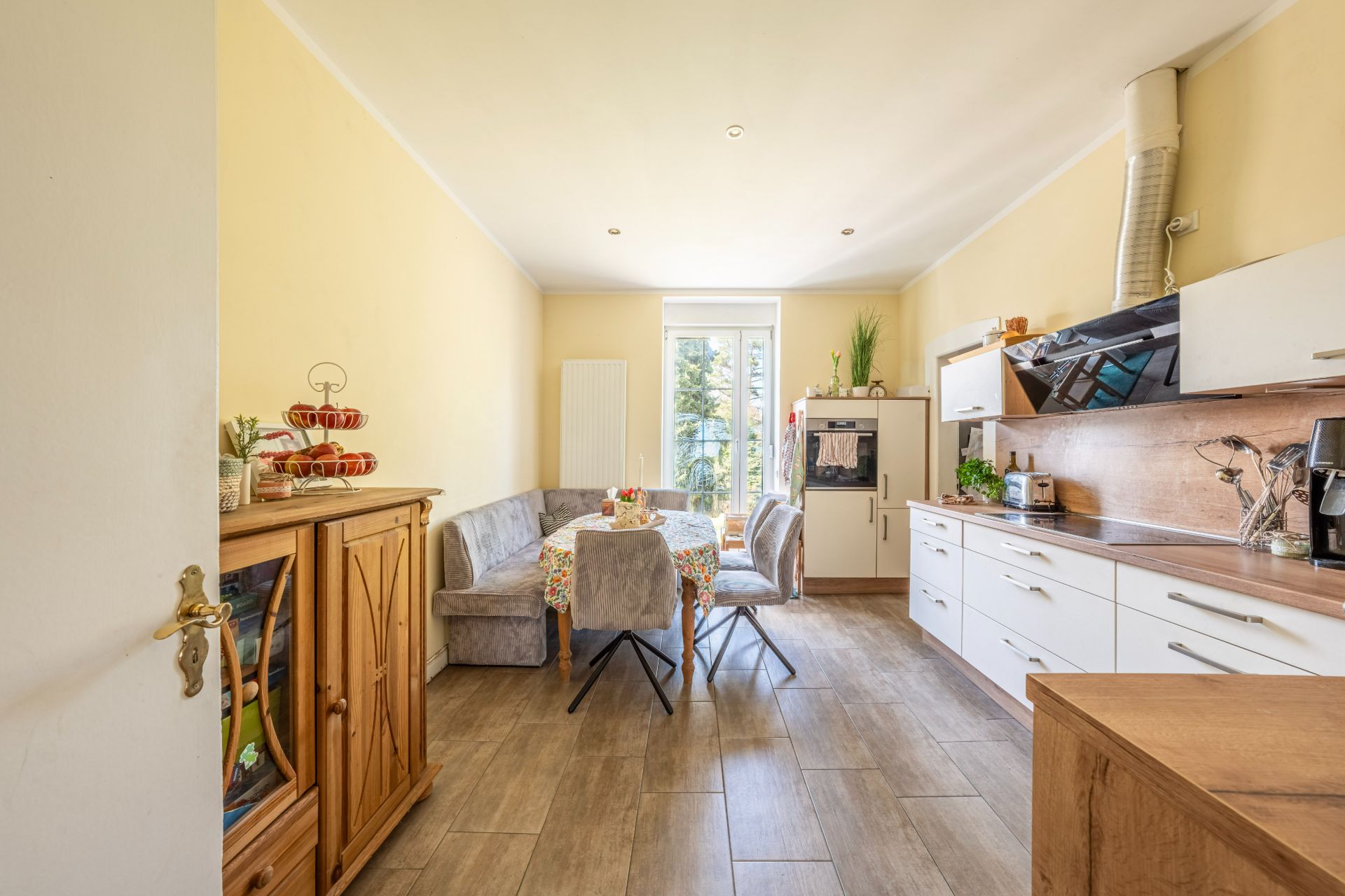 Helle Küche mit Esstisch, Eckbank, Schränken und Fenstertür zum Garten.