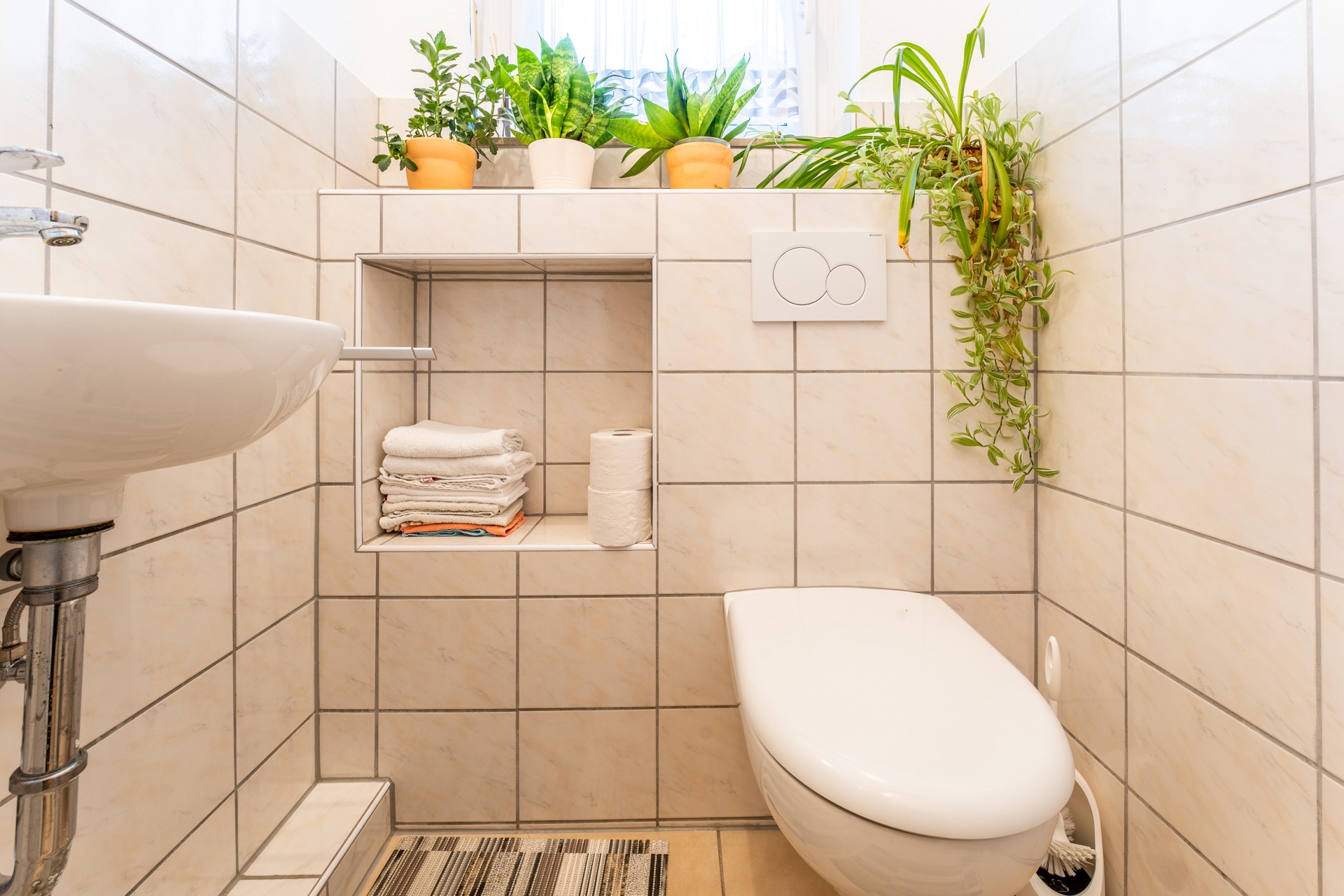 Modernes, gefliestes Badezimmer mit WC, Waschbecken, Pflanzen und Handtüchern.