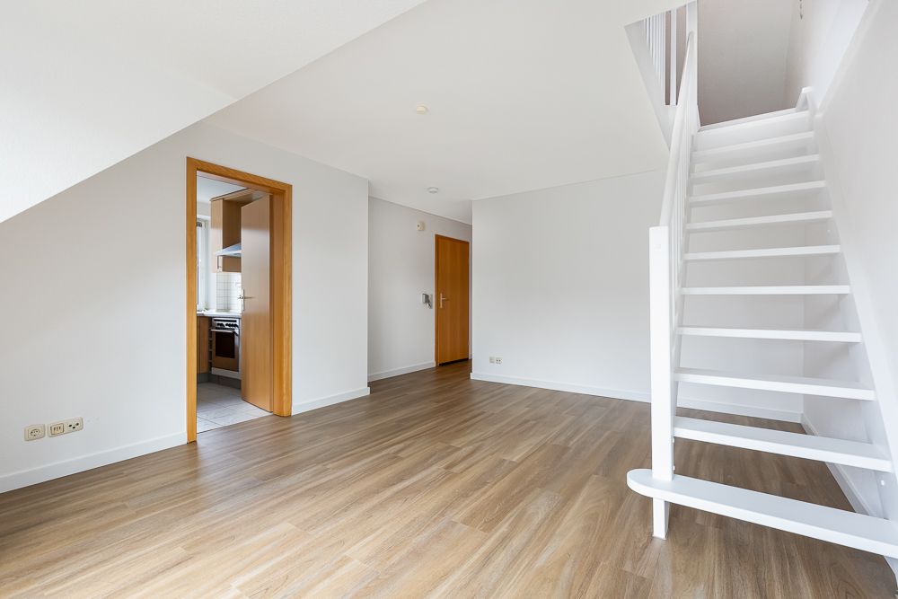 Helles Wohnzimmer mit Holzfußboden, offener Treppe und Zugang zur Küche.