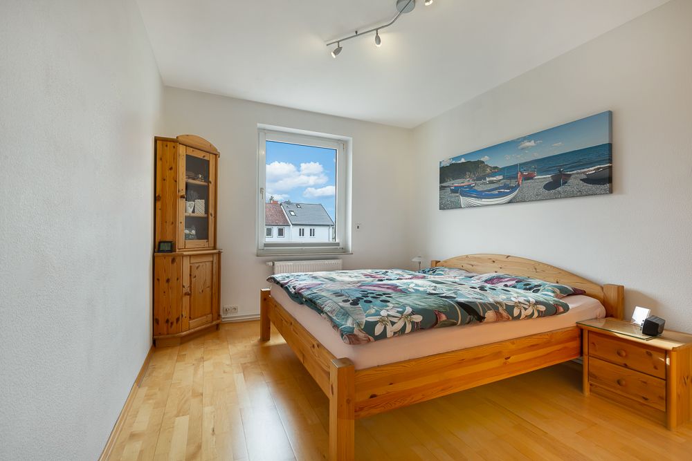 Schlafzimmer mit Holzbett, Nachttisch, Schrank und Fenster mit Blick nach draußen.