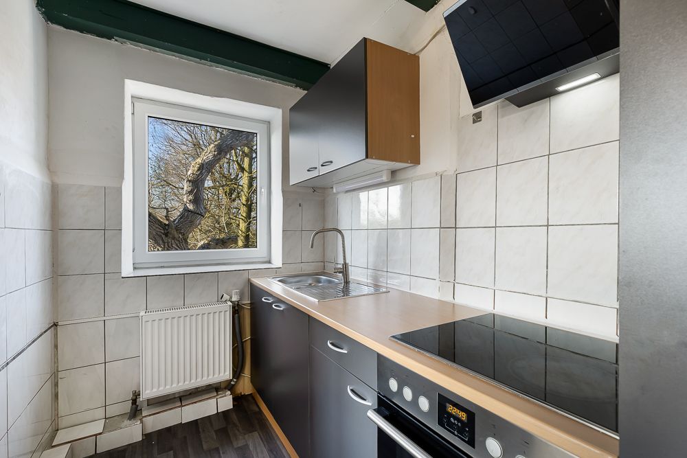 Kleine Küche mit Fenster, Spüle, Kochfeld, Backofen und weißen Wandfliesen.