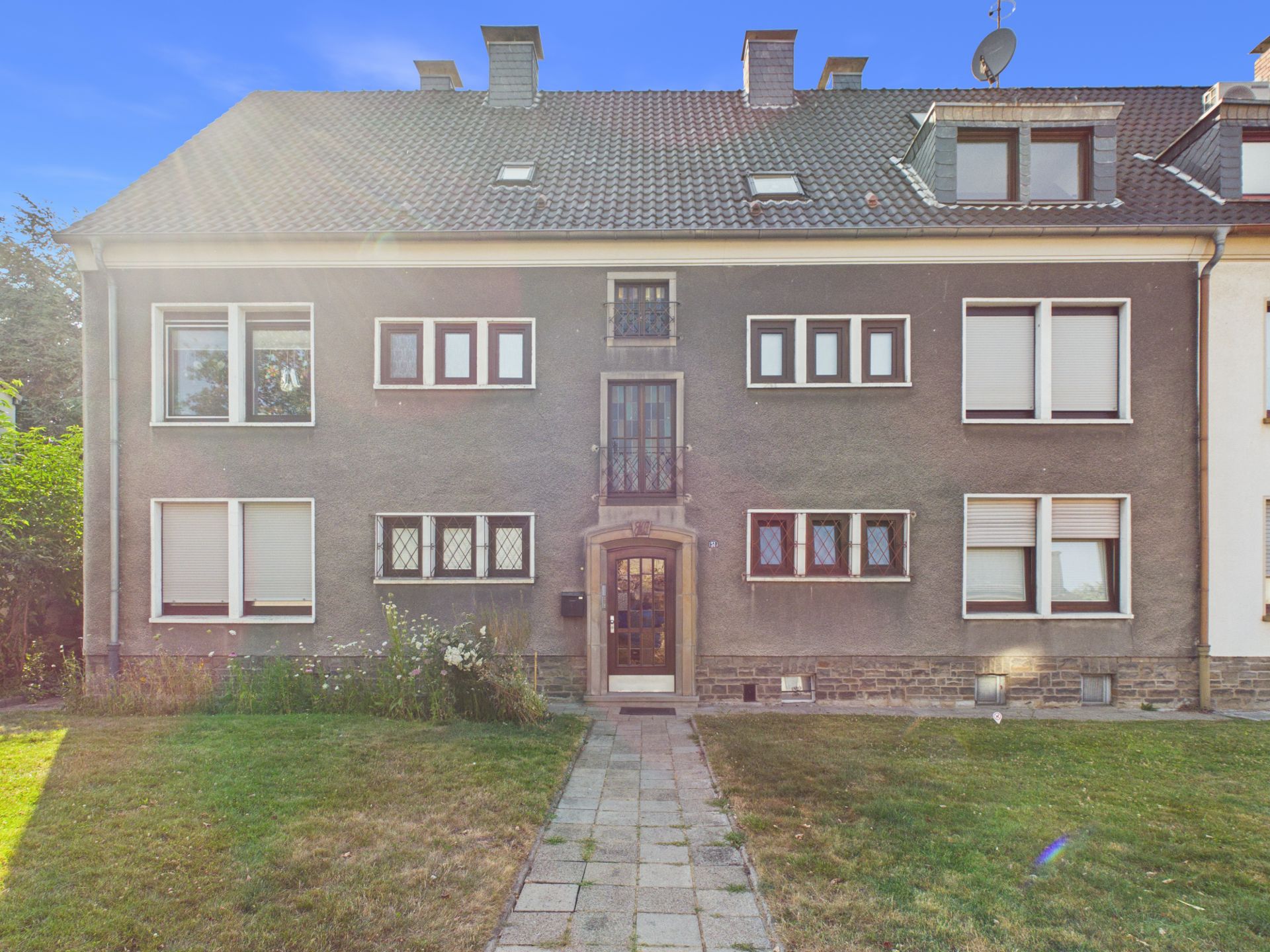 Vorderansicht eines mehrstöckigen Wohnhauses mit mehreren Fenstern und kleinem Vorgarten.