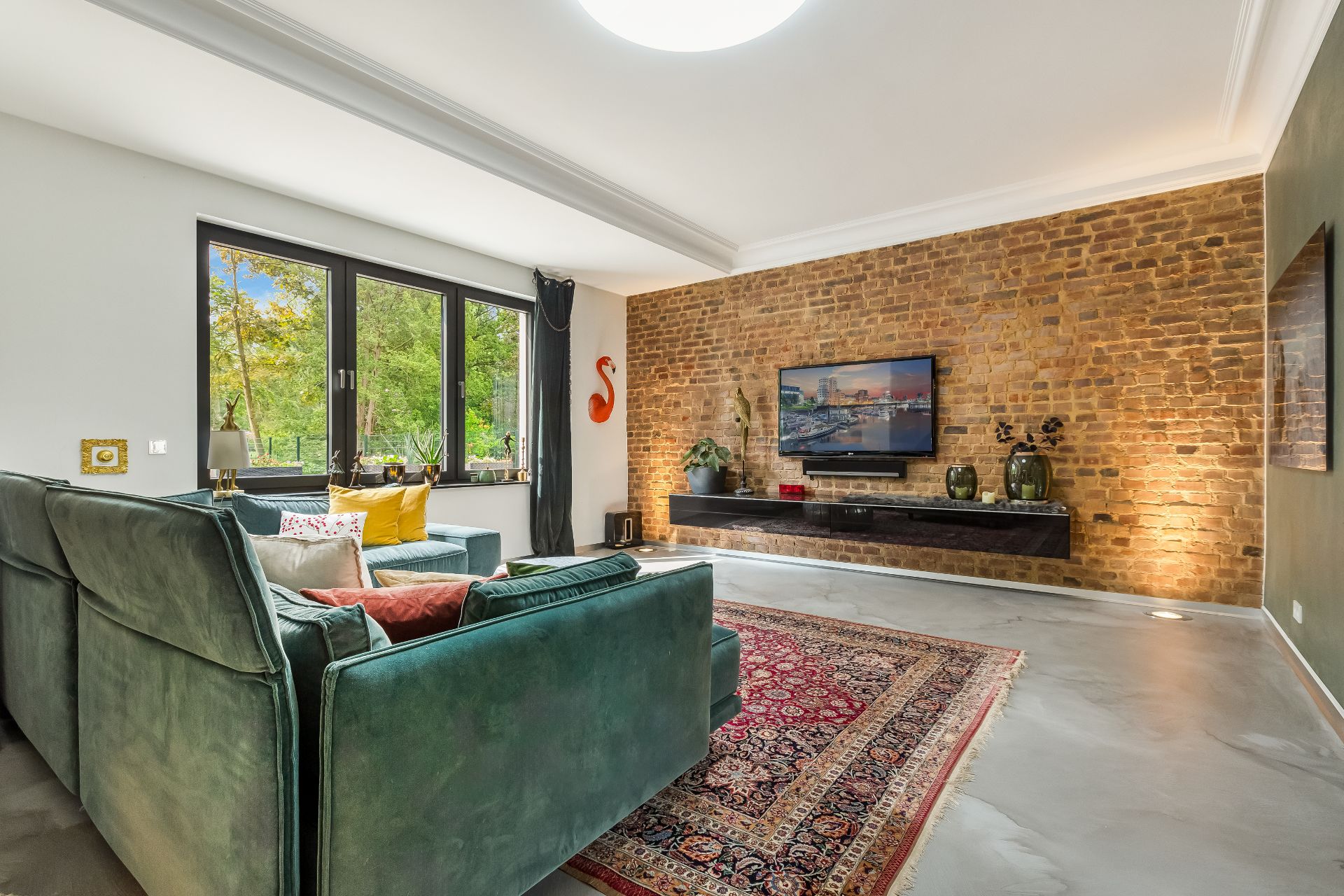 Modernes Wohnzimmer mit grüner Couch, gemauerter Wand, Teppich und großem Fenster.