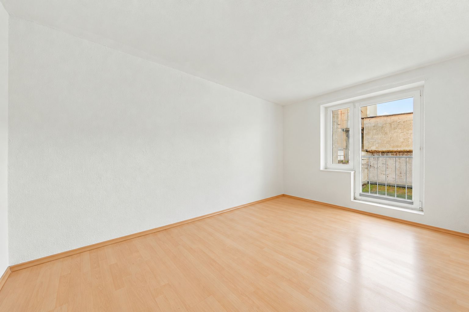 Leerer Raum mit hellem Holzfußboden und großem Fenster zur Außenseite.