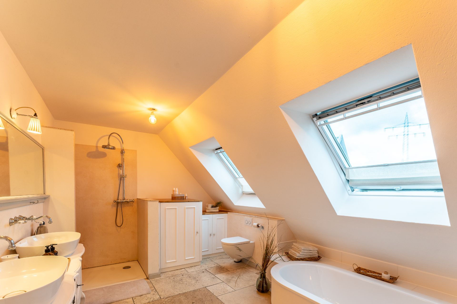 Helles Badezimmer mit Dachfenstern, Doppelwaschbecken, Dusche, Badewanne und WC.