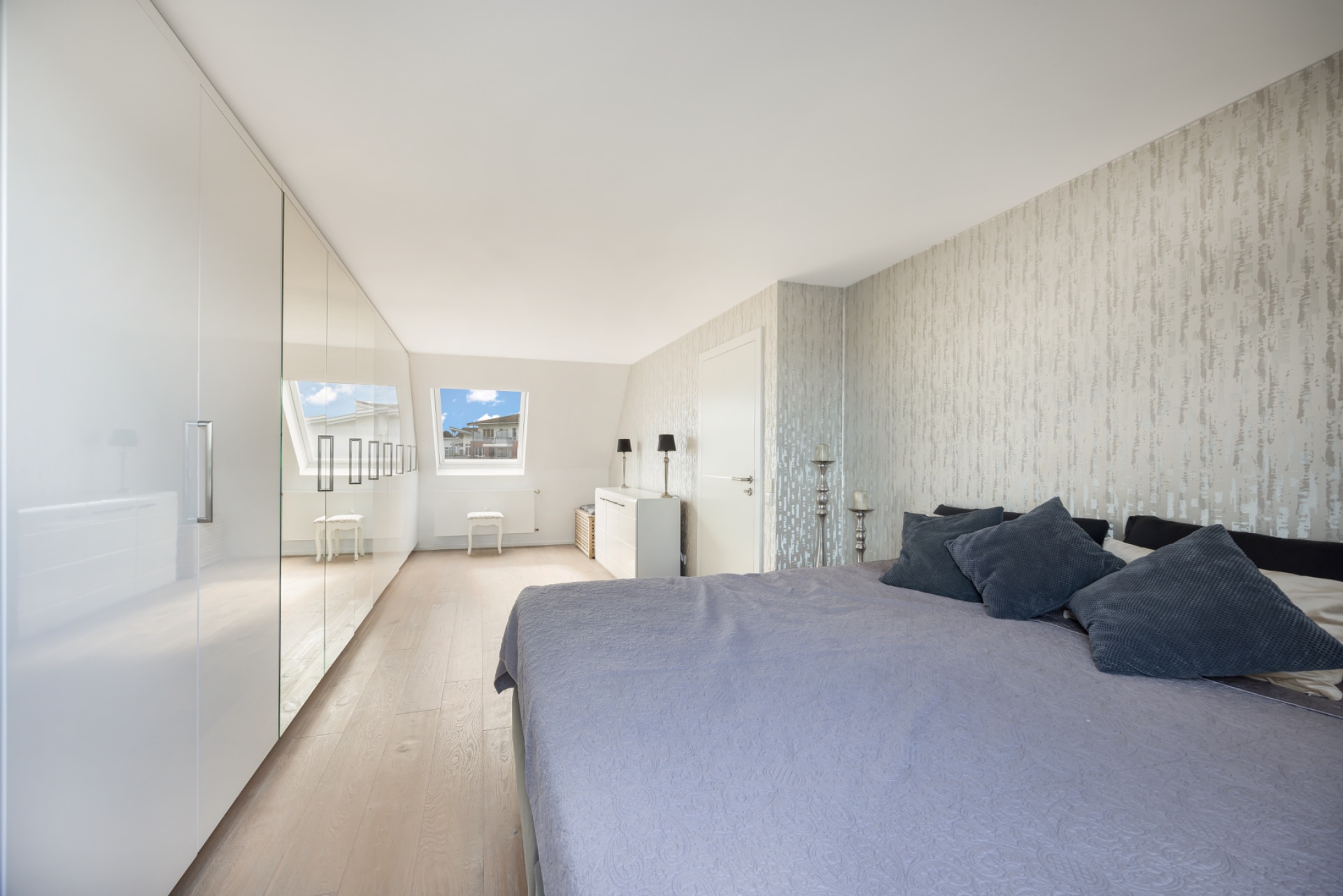 Modernes Schlafzimmer mit großem Bett, weißen Schränken und Fenster mit Blick nach draußen.
