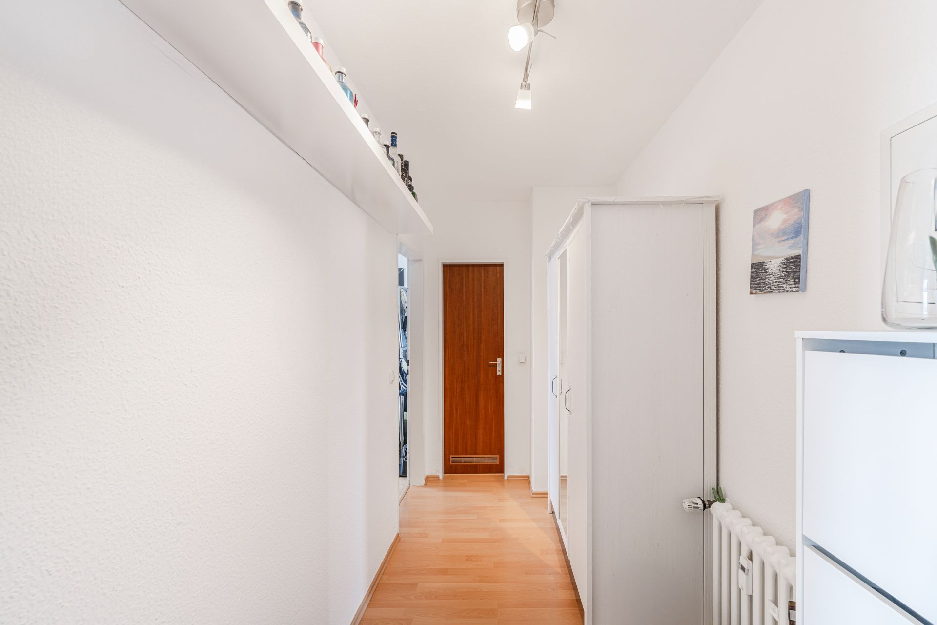 Heller Flur mit Holztür, weißem Schrank und Regal auf der linken Seite.