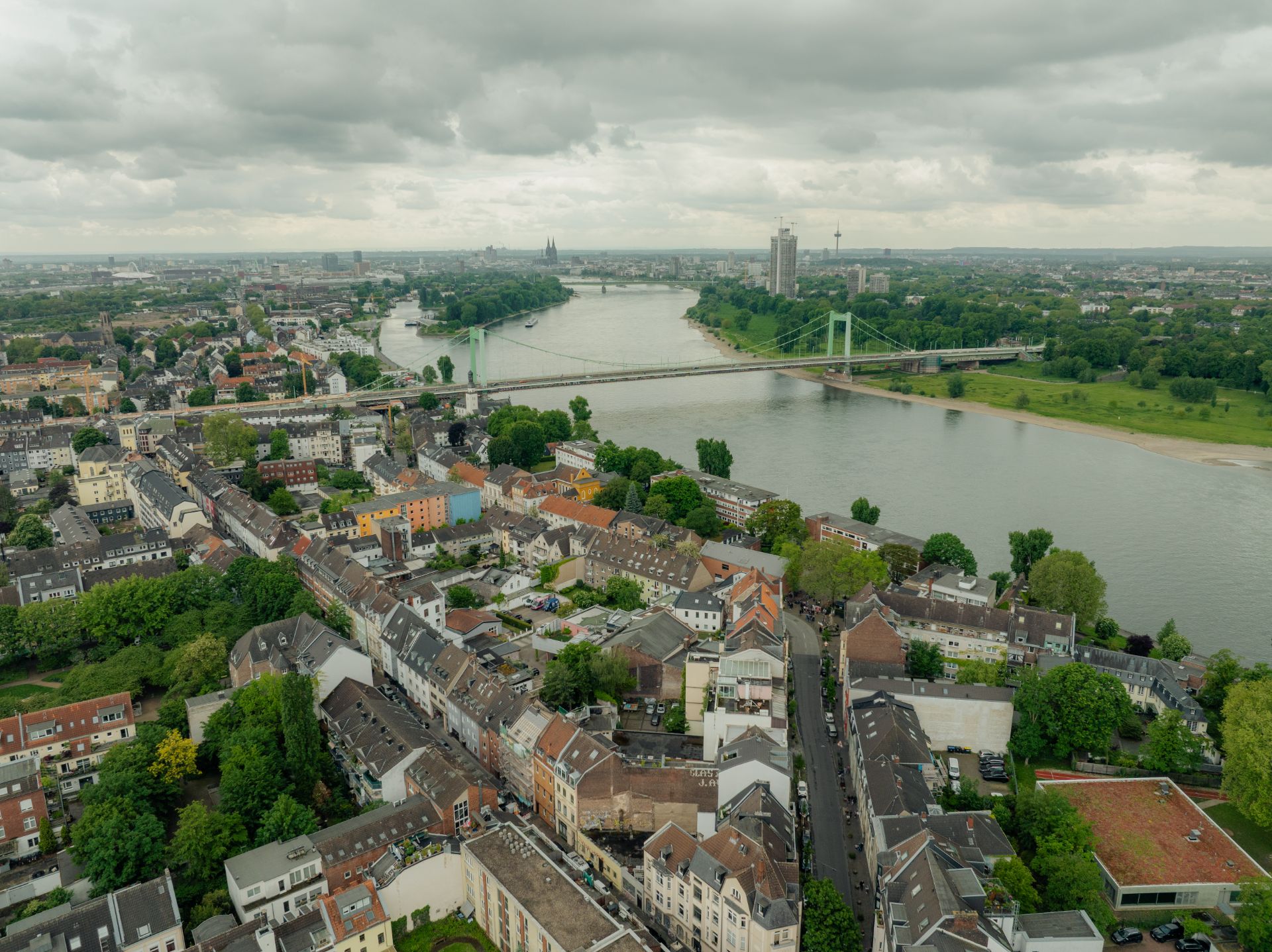 Luftaufnahme von Wohnhäusern, einer Brücke und einem Fluss unter bewölktem Himmel.