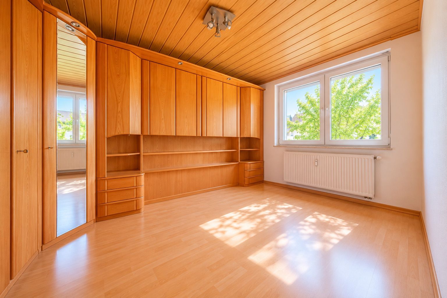 Helles Zimmer mit Holzschränken, Holzdecke, großem Fenster und Parkettboden.
