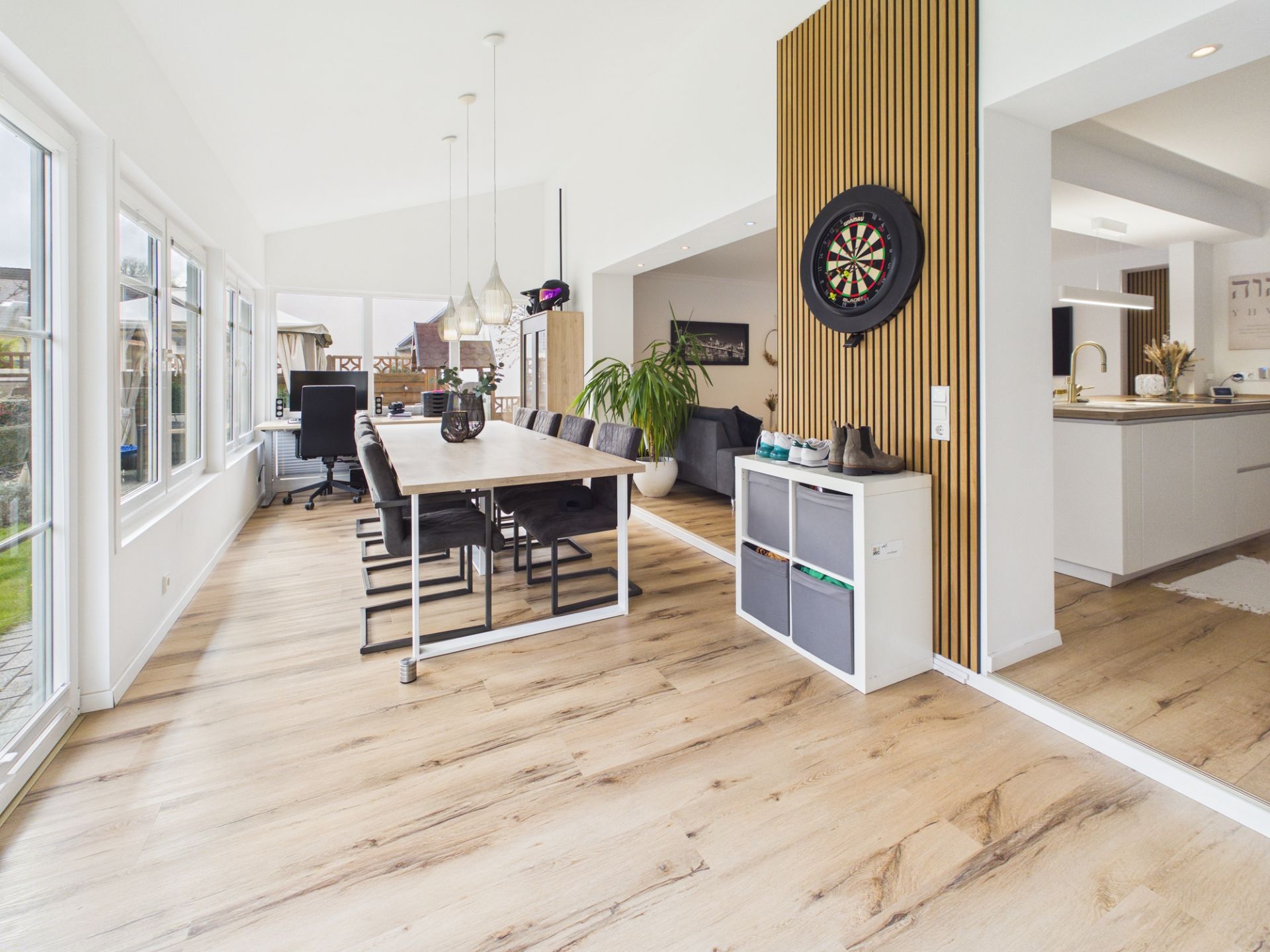 Helles Esszimmer mit langem Tisch, großen Fenstern und angrenzender moderner Küche.