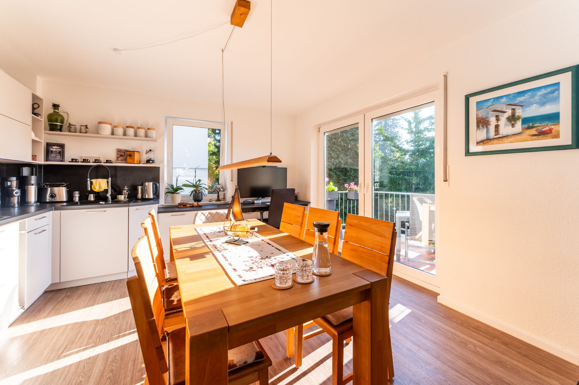 Helles Esszimmer mit Holztisch, sechs Stühlen, offener Küche und großen Fenstern zum Balkon.