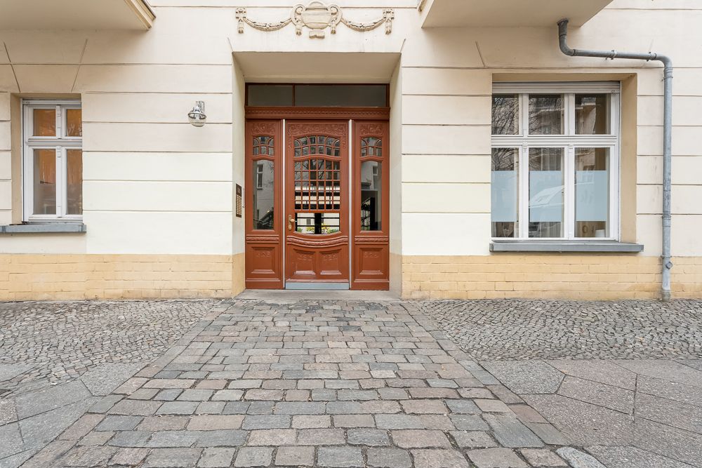 Eingangstür und zwei Fenster eines Wohnhauses aus hellem Putz mit Kopfsteinpflaster davor.