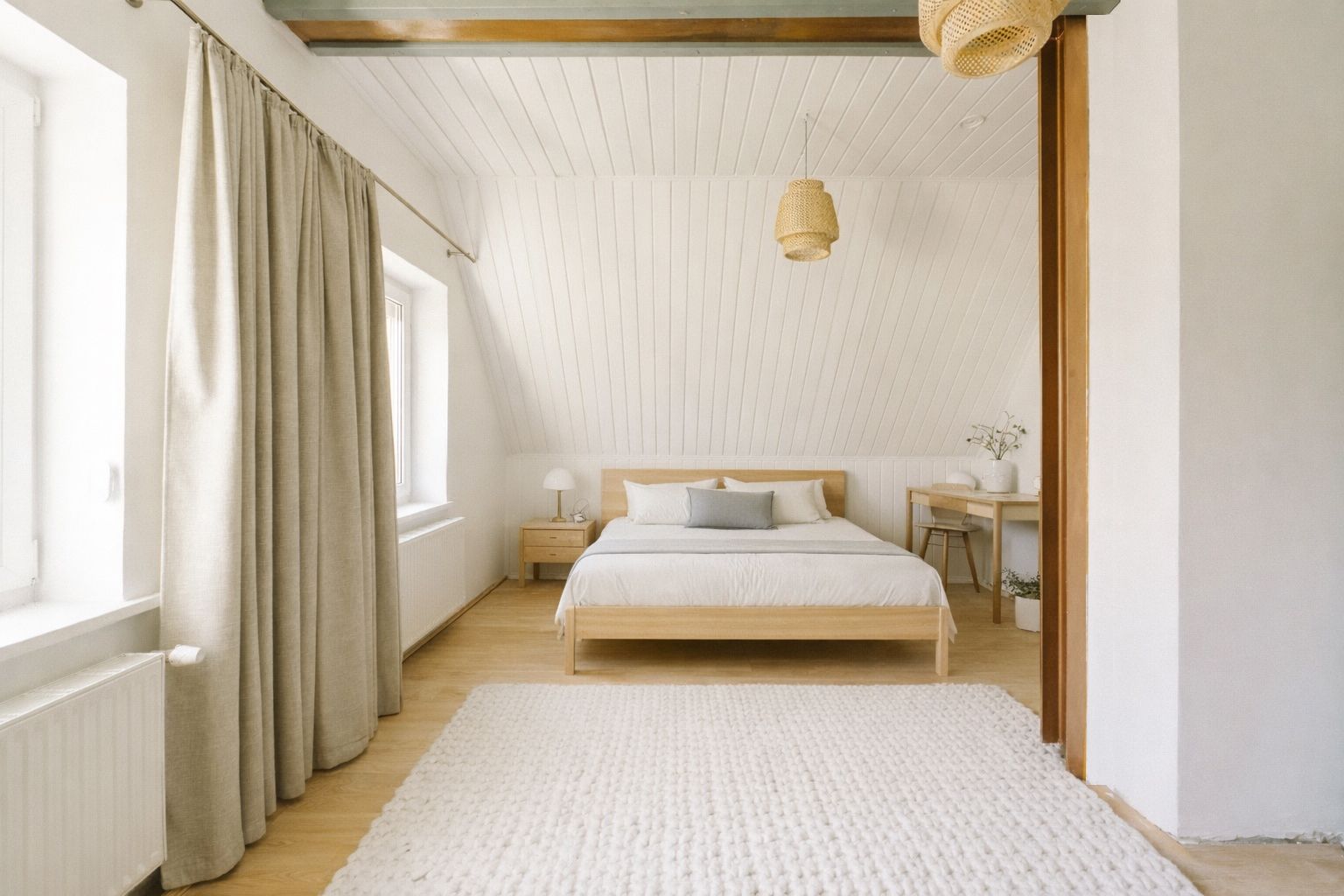 Helles Schlafzimmer mit Holzbett, Nachttischen, Schreibtisch und großen Fenstern.