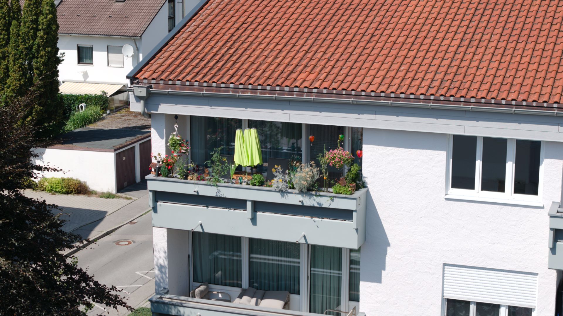 Balkon eines Wohnhauses mit Blumen, Pflanzen und einem grünen Handtuch am Geländer.