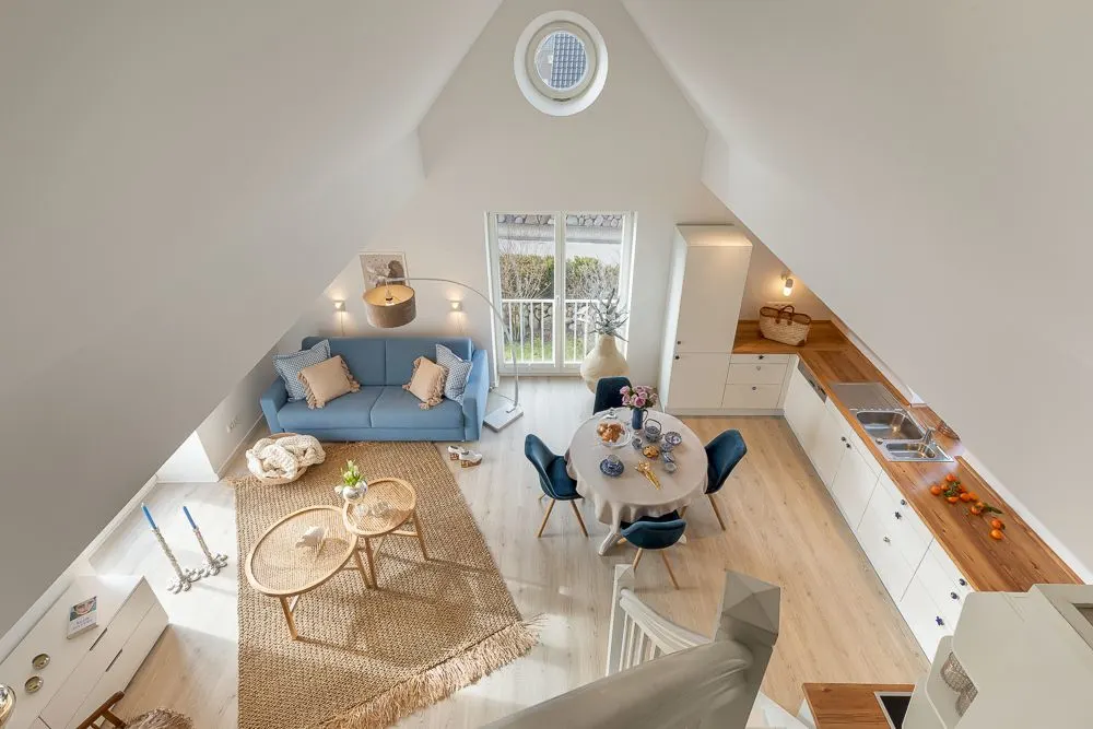 Wohnzimmer mit blauem Sofa, Esstisch und offener Küche in heller Dachgeschosswohnung.