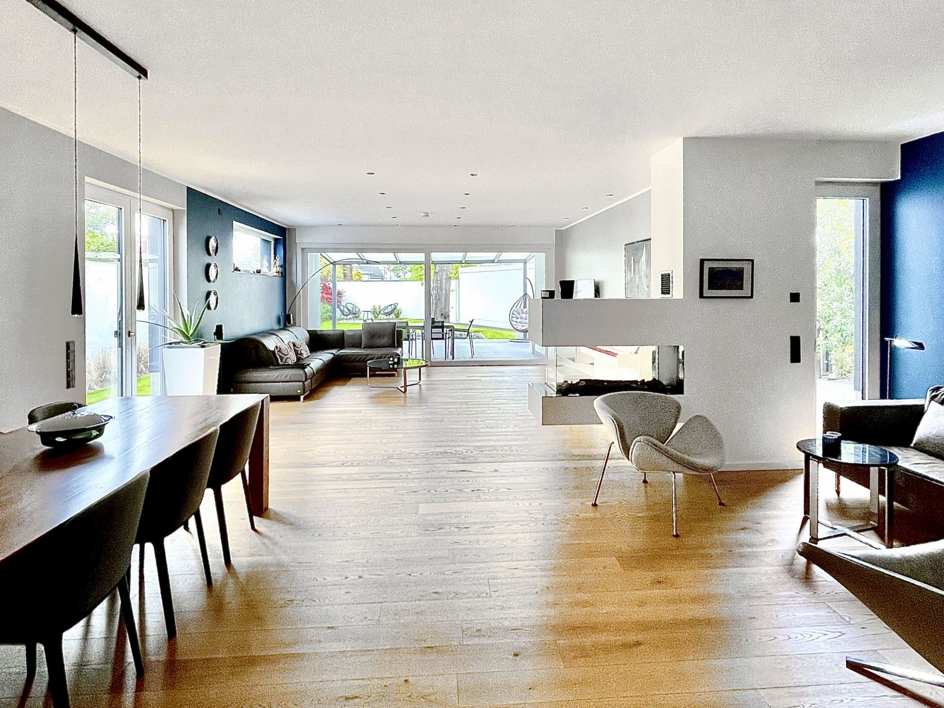 Helles Wohnzimmer mit Holzboden, Essbereich, Sofas und großem Fenster zum Garten.