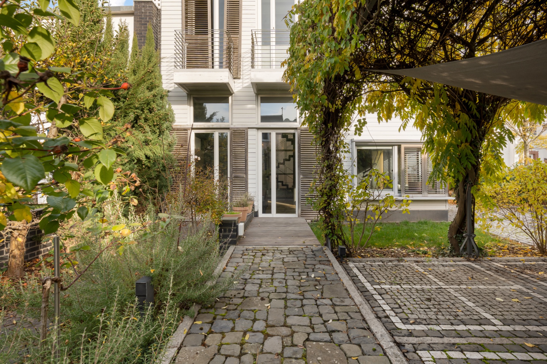 Gepflasterter Weg führt durch einen Garten zu einem modernen Wohnhaus mit großen Fenstern.