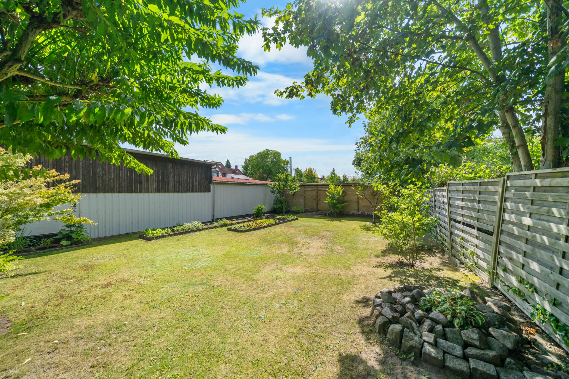 Garten mit Rasenfläche, Blumenbeeten, Bäumen und Holzzaun an der Seite.