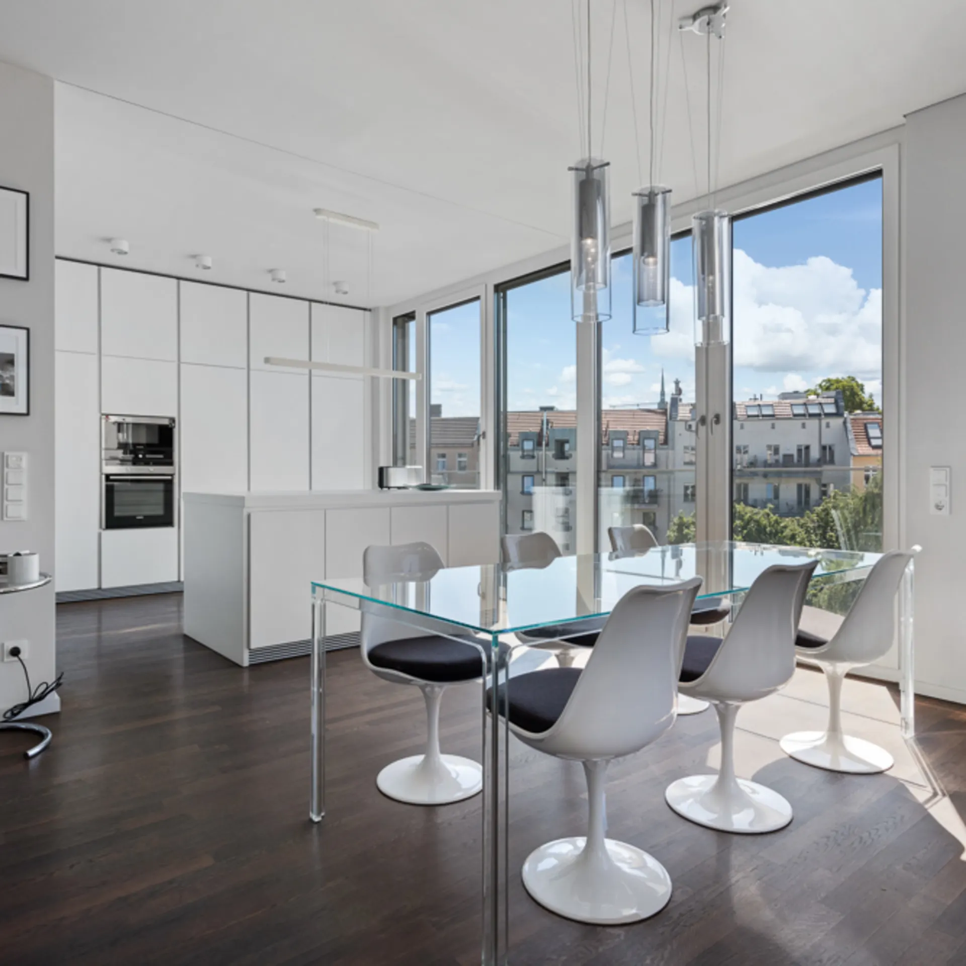 Heller Essbereich mit Glastisch, sechs weißen Stühlen und großer Fensterfront zur Stadt.