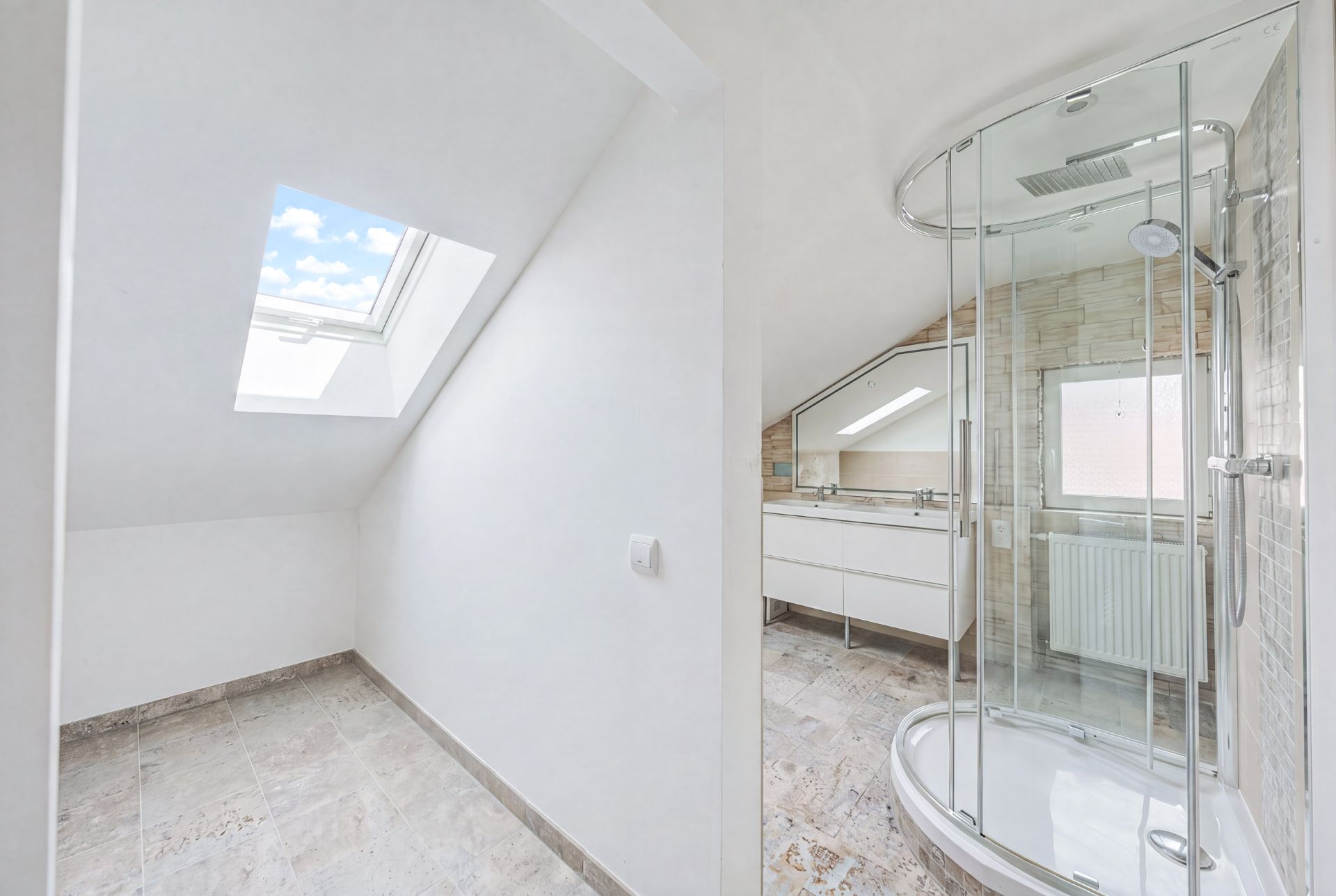 Modernes Badezimmer mit Dusche, großem Spiegel und Dachfenster, Fliesenboden und viel Tageslicht.
