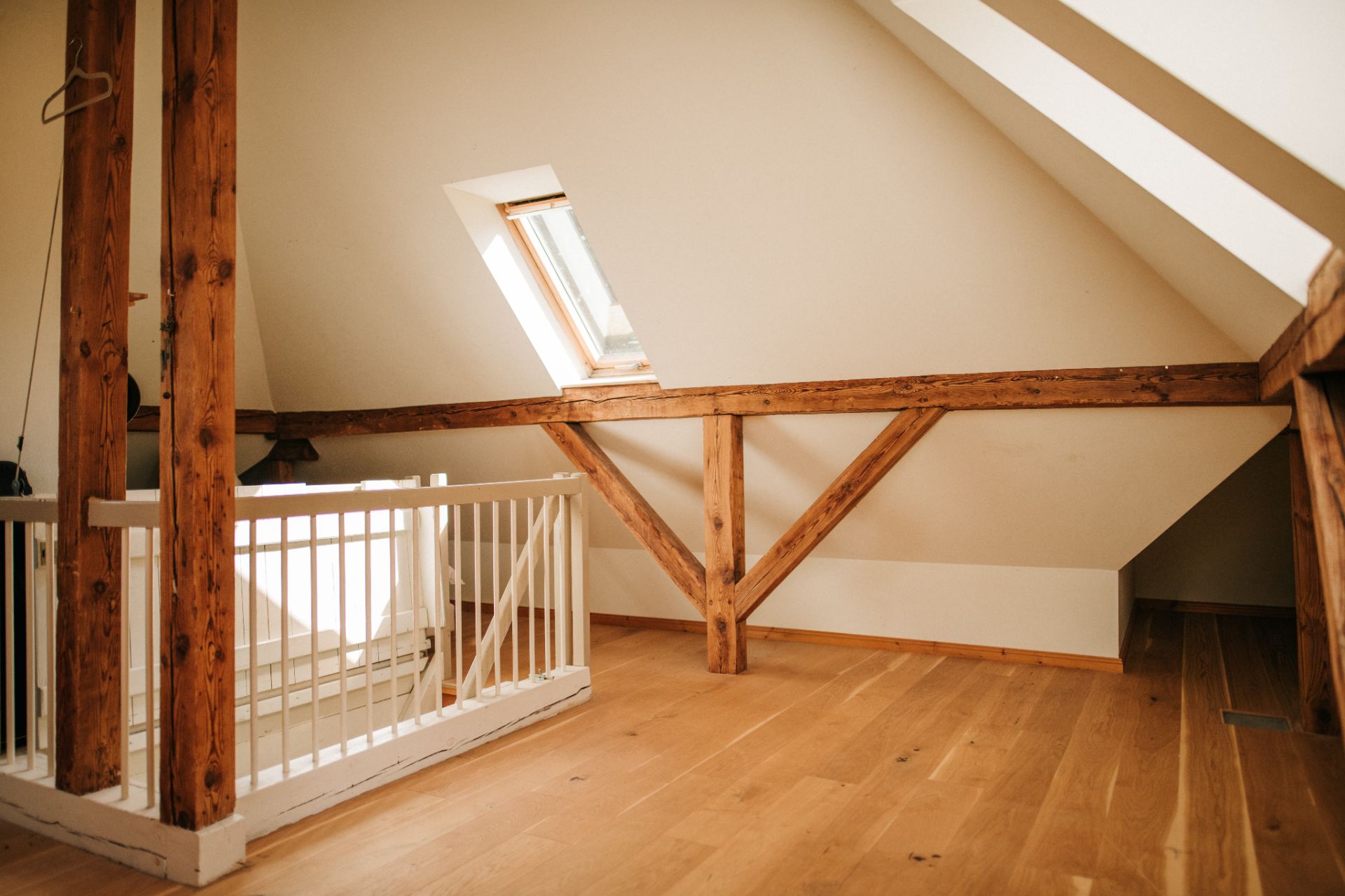 Heller Dachbodenraum mit Holzträgern, weißer Brüstung und Dachfenster.