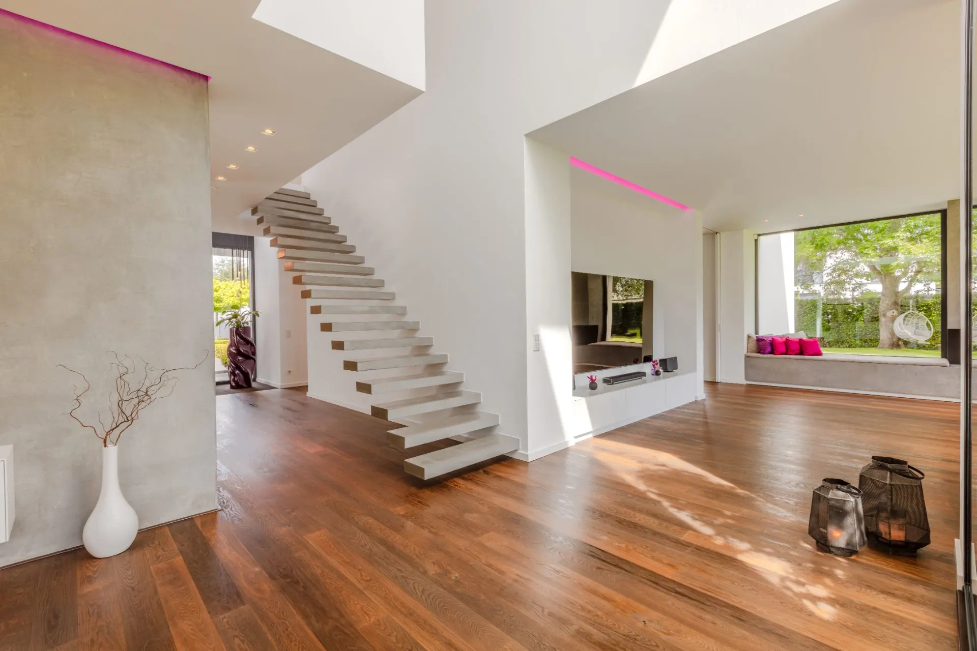 Modernes Wohnzimmer mit Holzfußboden, freitragender Treppe und großen Fenstern.