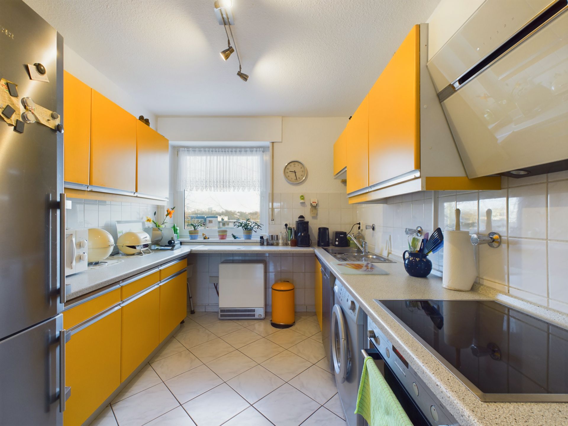 Moderne Küche mit gelben Schränken, Fenster, Haushaltsgeräten und weißen Fliesen.