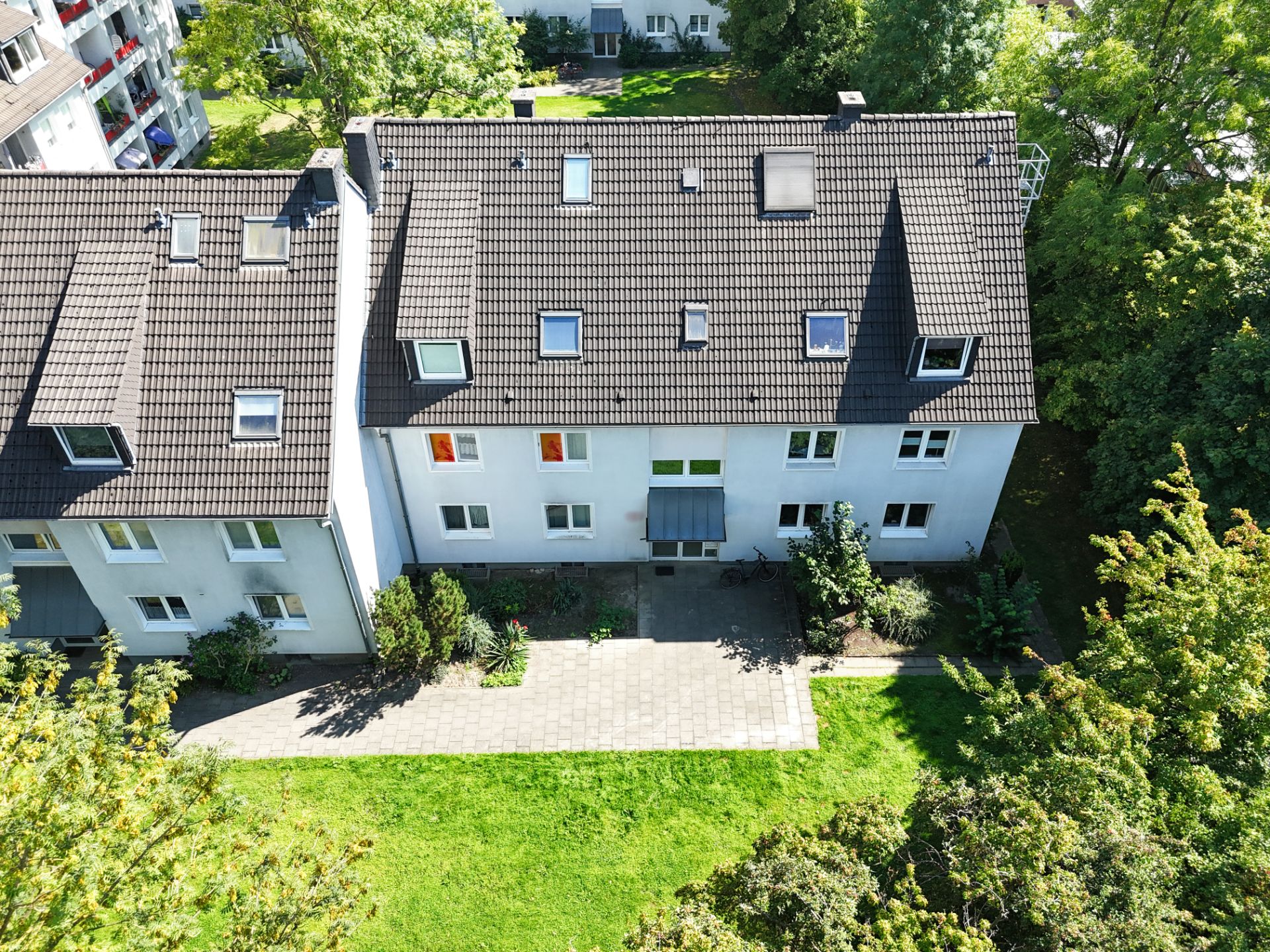 Wohnhaus mit dunklem Dach, mehreren Fenstern und kleinem Vorgarten, von oben fotografiert.