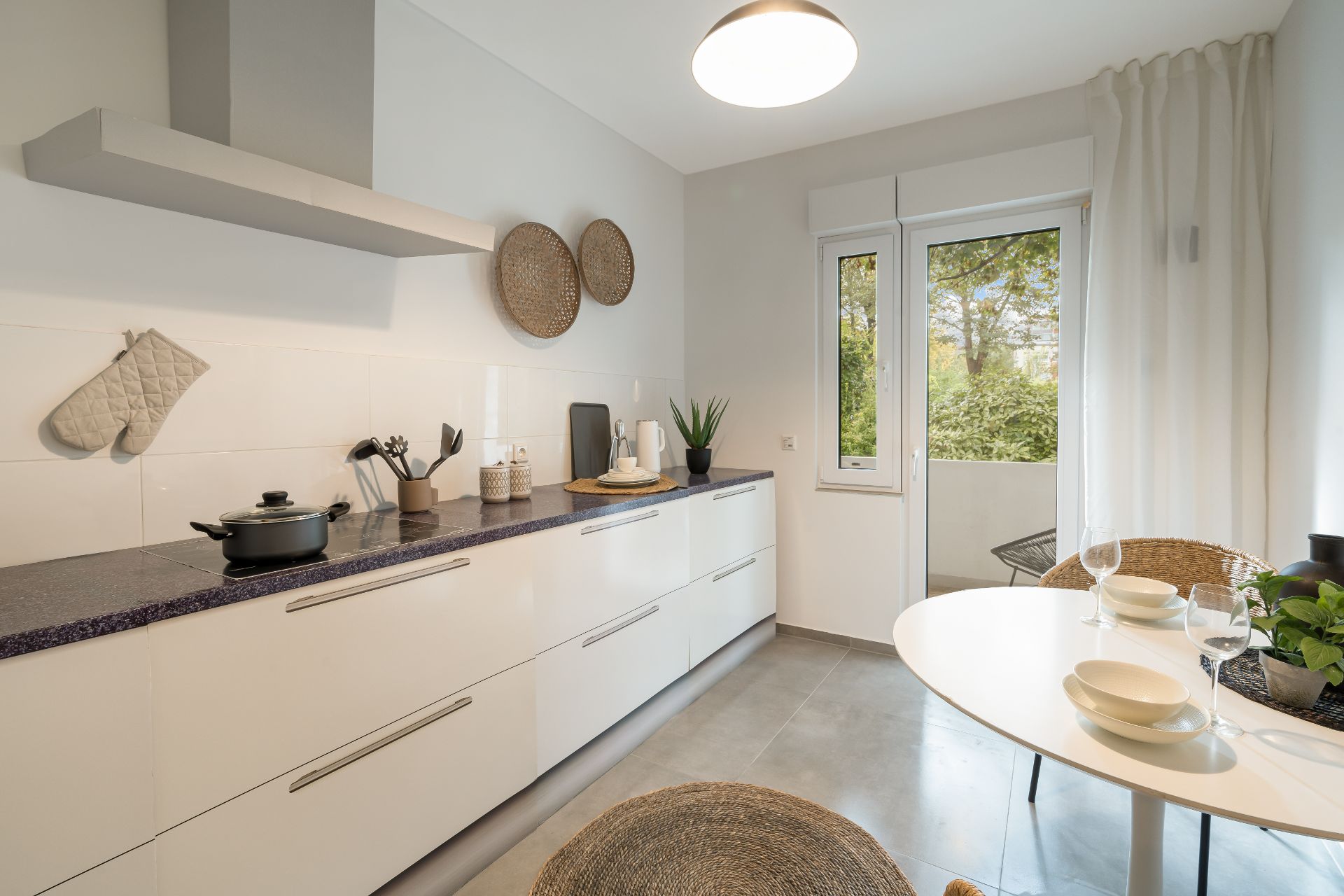 Moderne helle Küche mit Esstisch, Stühlen und Blick auf Garten durch Fenster und Tür.