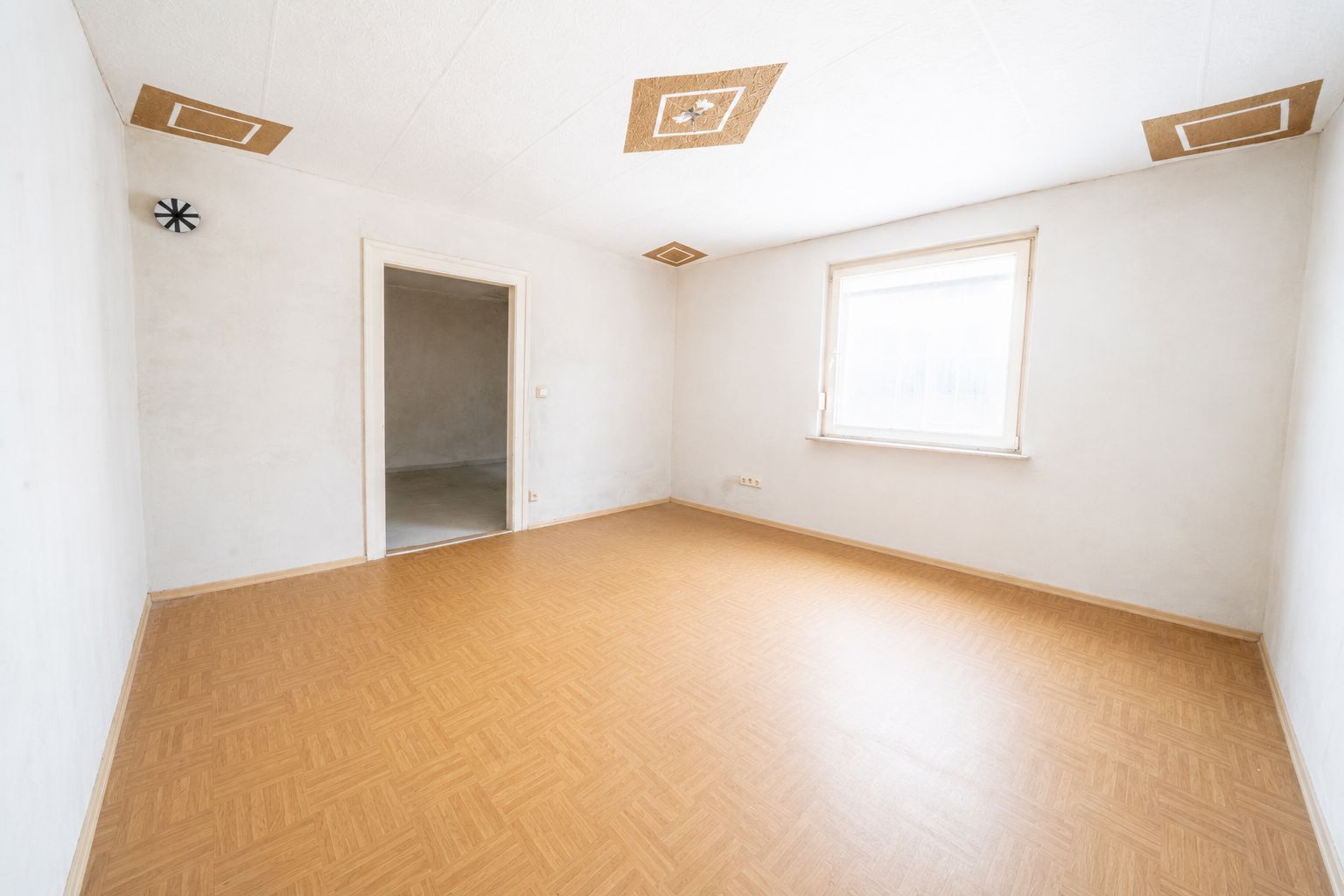 Helles, leeres Zimmer mit Holzfußboden, weißer Wand, Fenster und Tür.