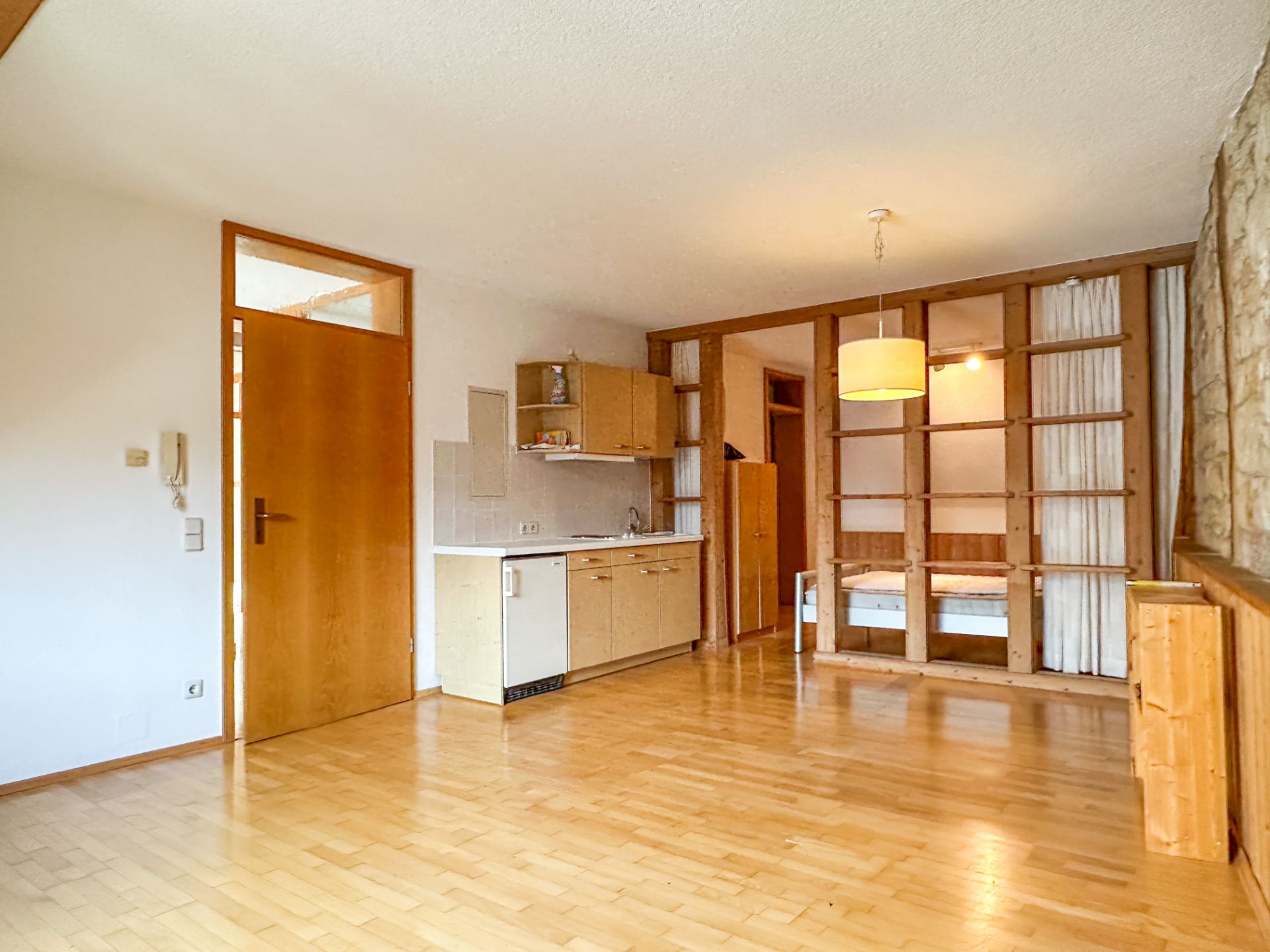 Heller Wohnraum mit offener Küche, Holzfußboden und abgetrenntem Schlafbereich mit Bett.