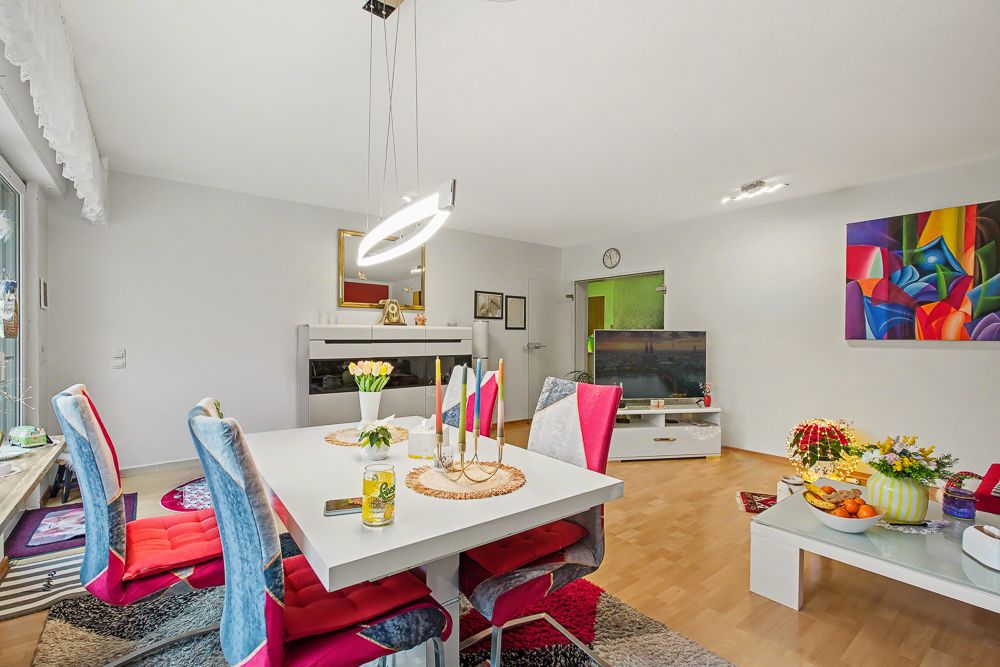 Modernes Wohnzimmer mit Esstisch, bunten Stühlen und Fernseher auf Parkettboden.