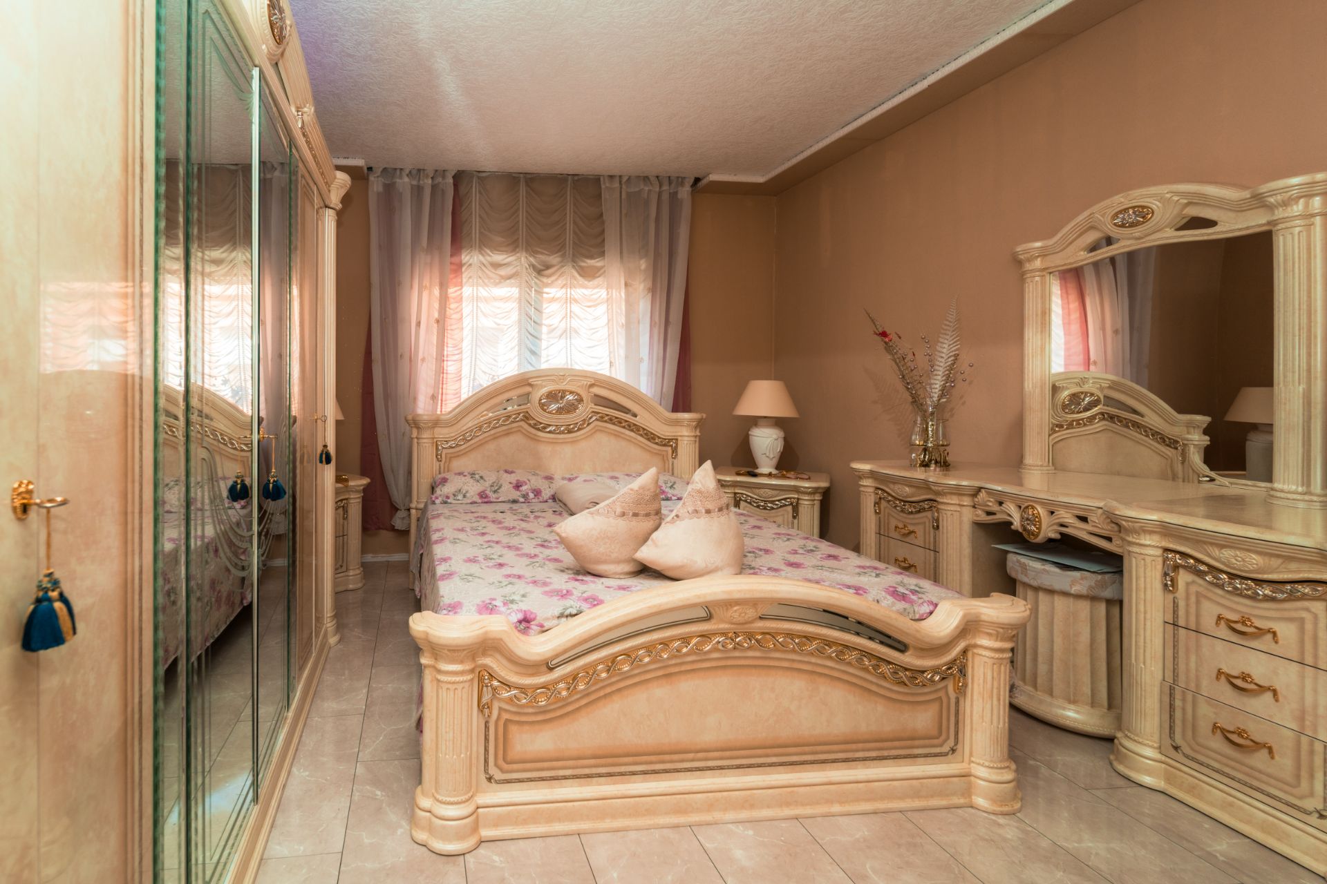 Schlafzimmer mit großem Bett, Spiegel-Schrank, Kommode mit Spiegel und zwei Fenstern mit Vorhängen.