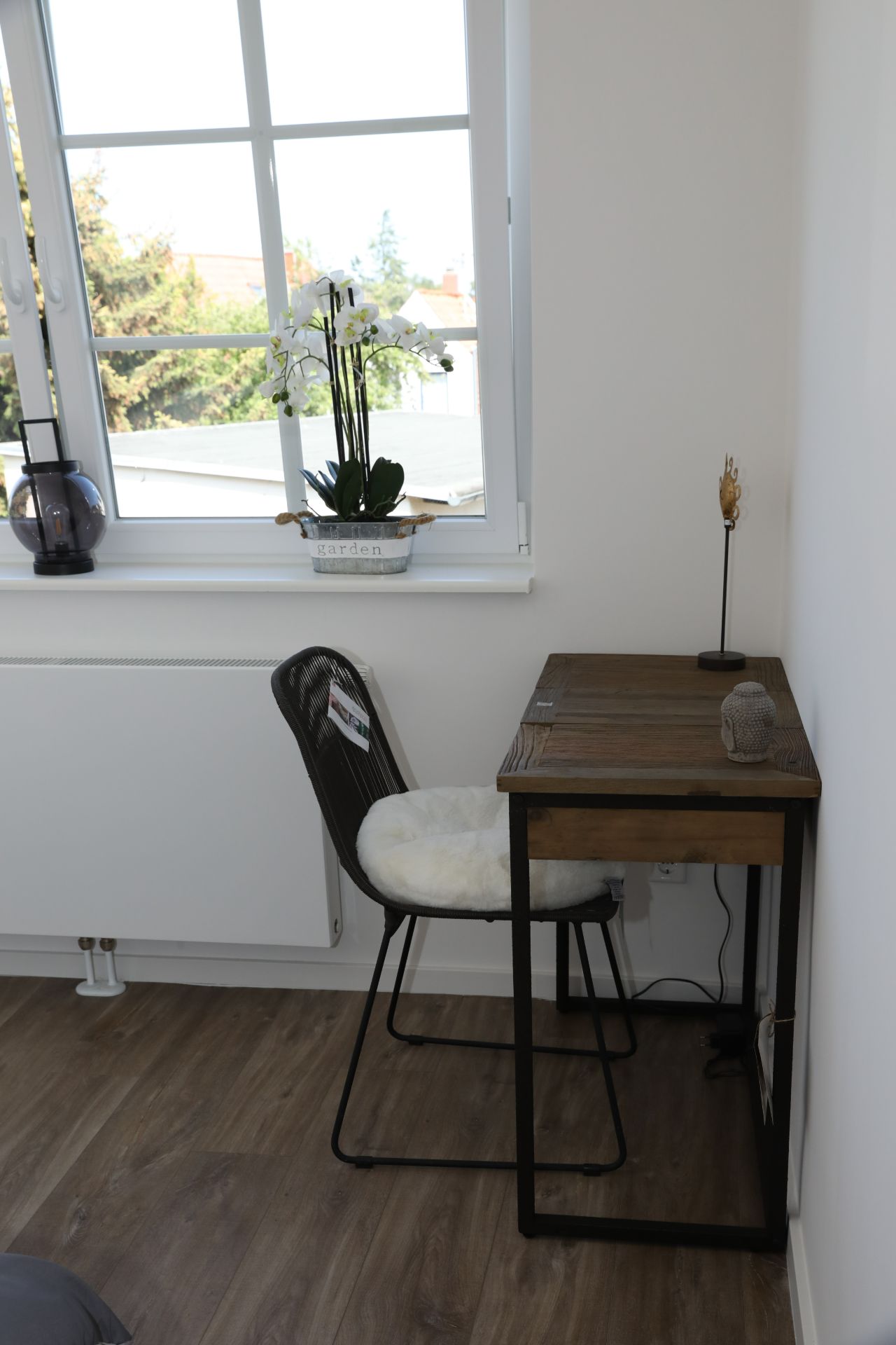 Kleiner Schreibtisch mit Stuhl vor Fenster, Blume und Lampe auf Fensterbrett.