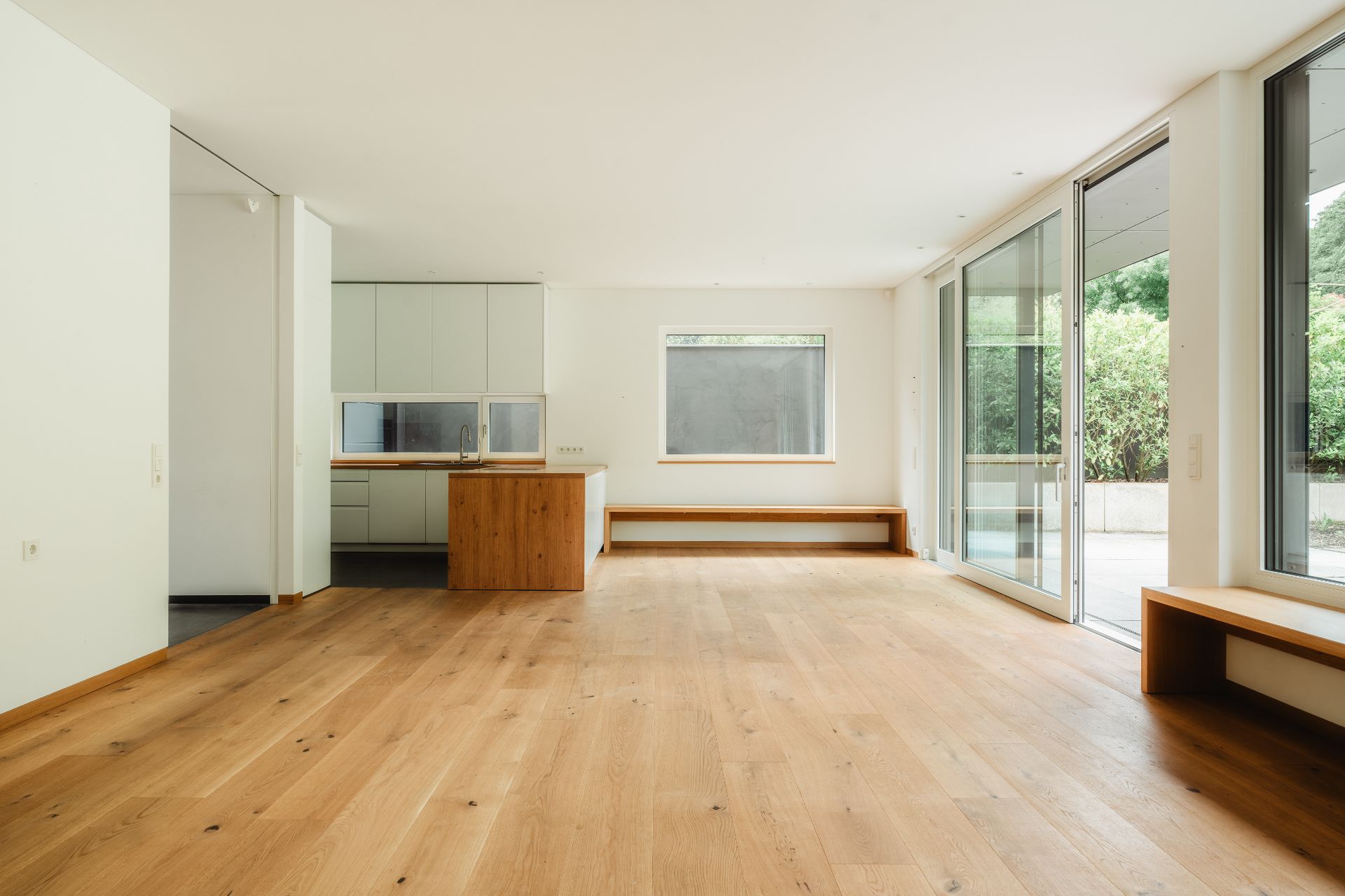 Helles Wohnzimmer mit Holzfußboden, offener Küche und großen Fenstern zum Garten.