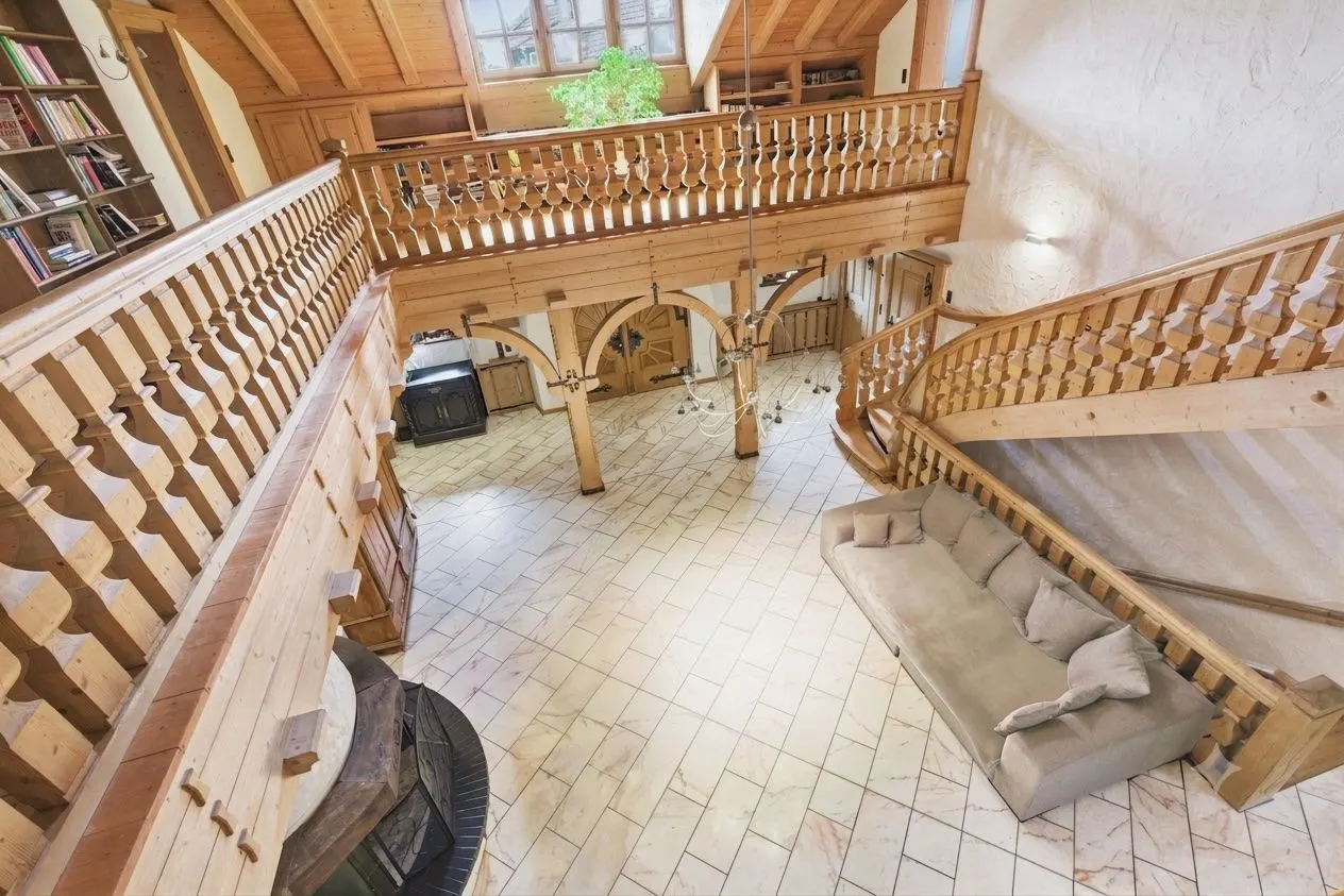 Großes Wohnzimmer mit Holzgeländer, Kamin, Sofa und Fliesenboden, Blick von oben.