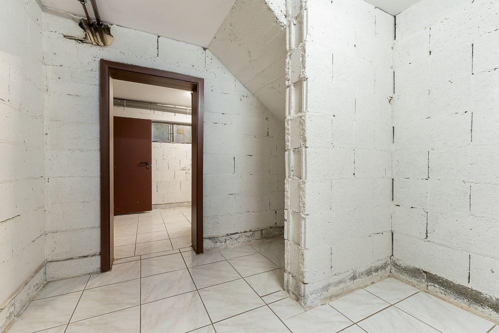 Rohbaukeller mit weißen Wänden und gefliesten Böden, Tür führt in einen weiteren Raum.