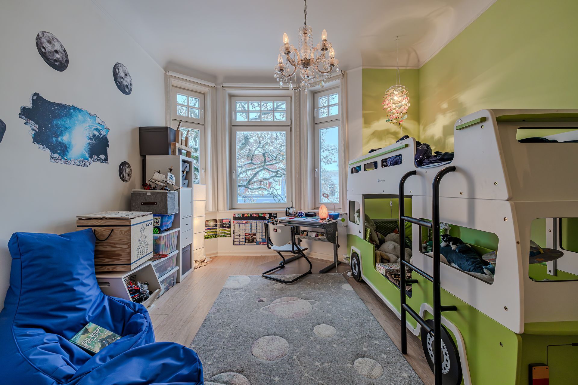 Kinderzimmer mit Hochbett in Bus-Optik, Schreibtisch, Spielsachen und großen Fenstern.