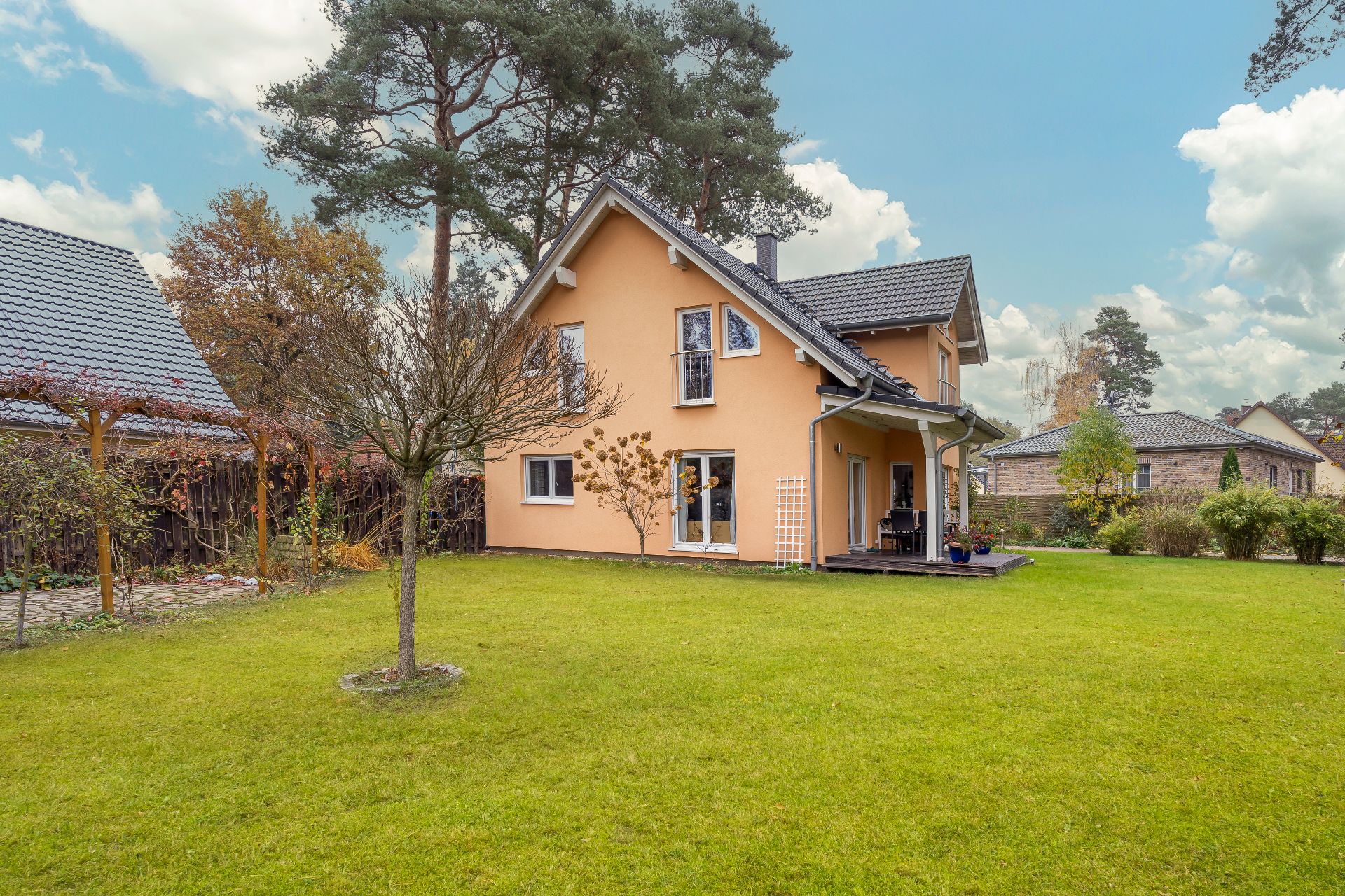 Modernes Einfamilienhaus mit großem Garten, Terrasse und umliegenden Bäumen.
