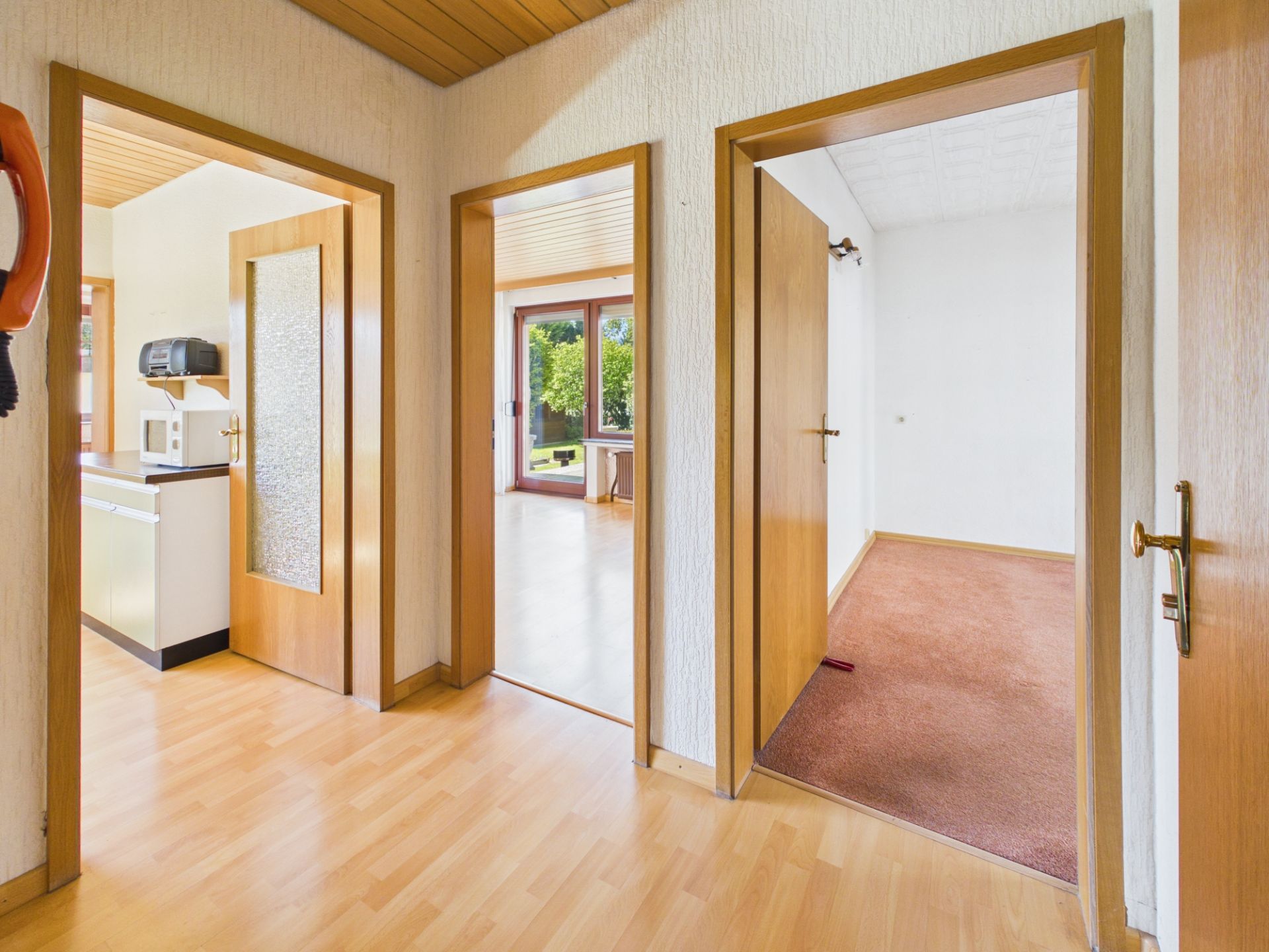 Flur mit drei offenen Türen zu Küche, Wohnzimmer und leerem Zimmer, Holzboden und Holztüren.