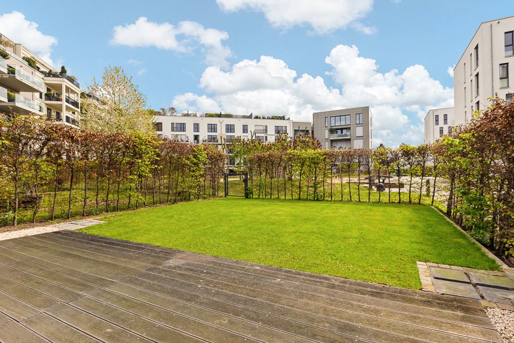 Grüne Terrasse mit Rasen und Hecke, umgeben von modernen Wohngebäuden.