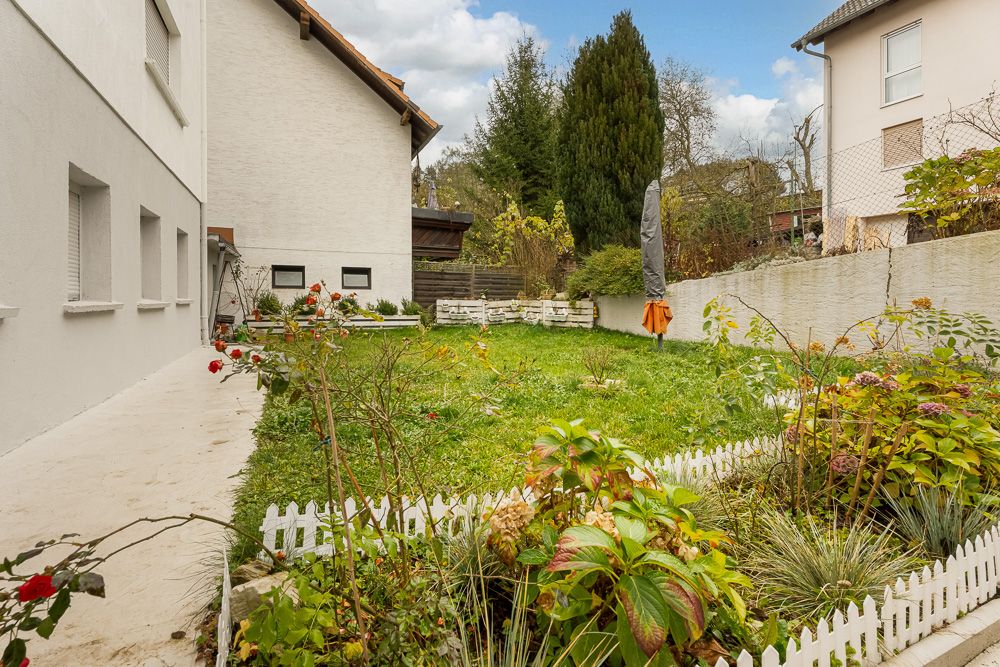Gepflegter Garten mit Rasen, Blumenbeeten und kleinem weißen Gartenzaun an einem Wohnhaus.