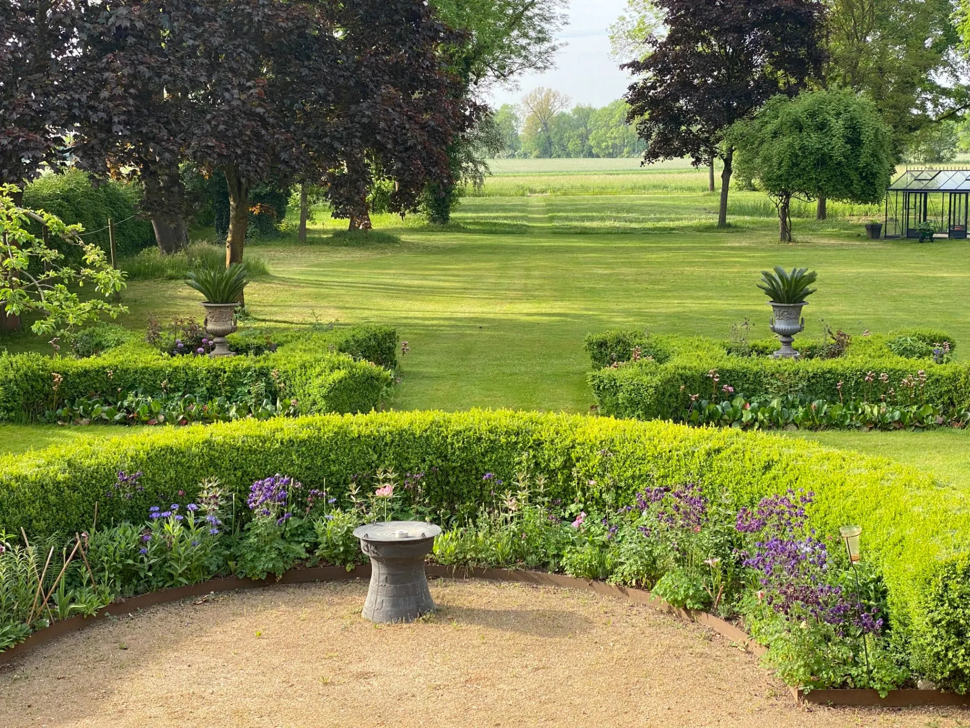 Gepflegter Garten mit Blumenbeeten, Hecken, Rasenfläche und Bäumen im Hintergrund.